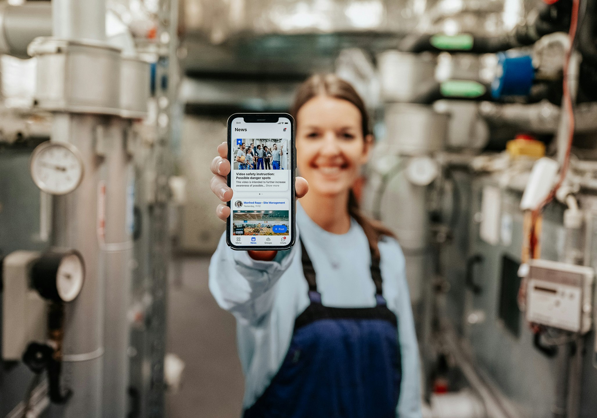 Woman holding mobile phone with Flip app on display and production hall in the background