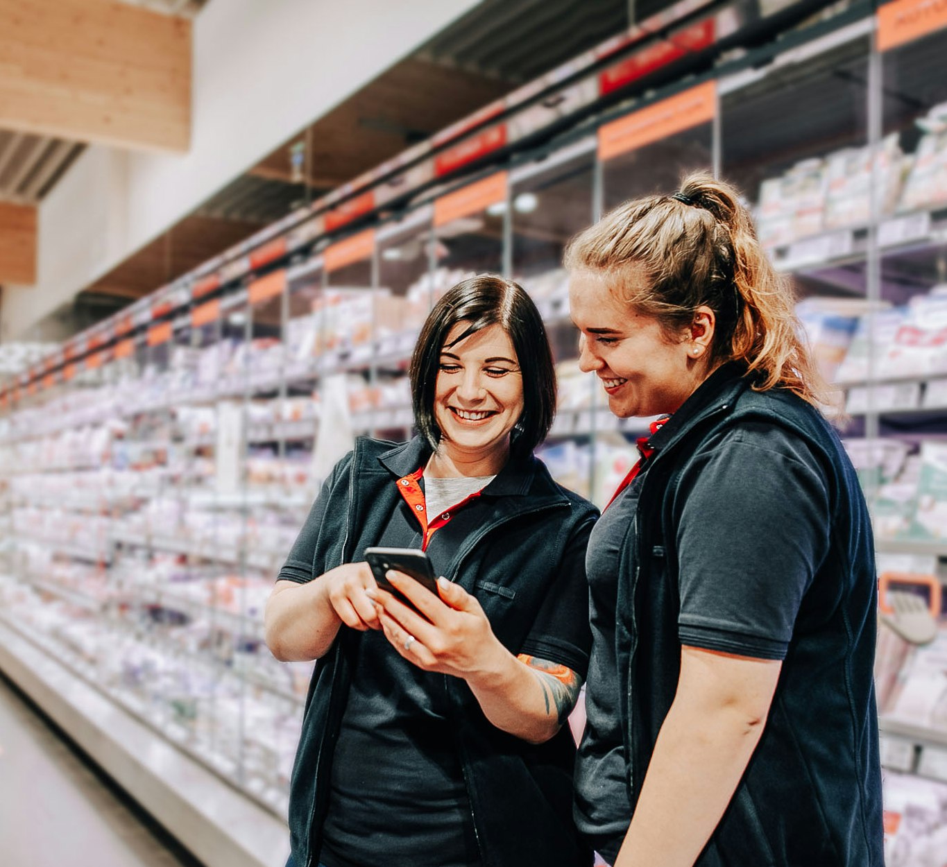 Zwei weibliche REWE Angestellte schauen auf ein Mobiltelefon