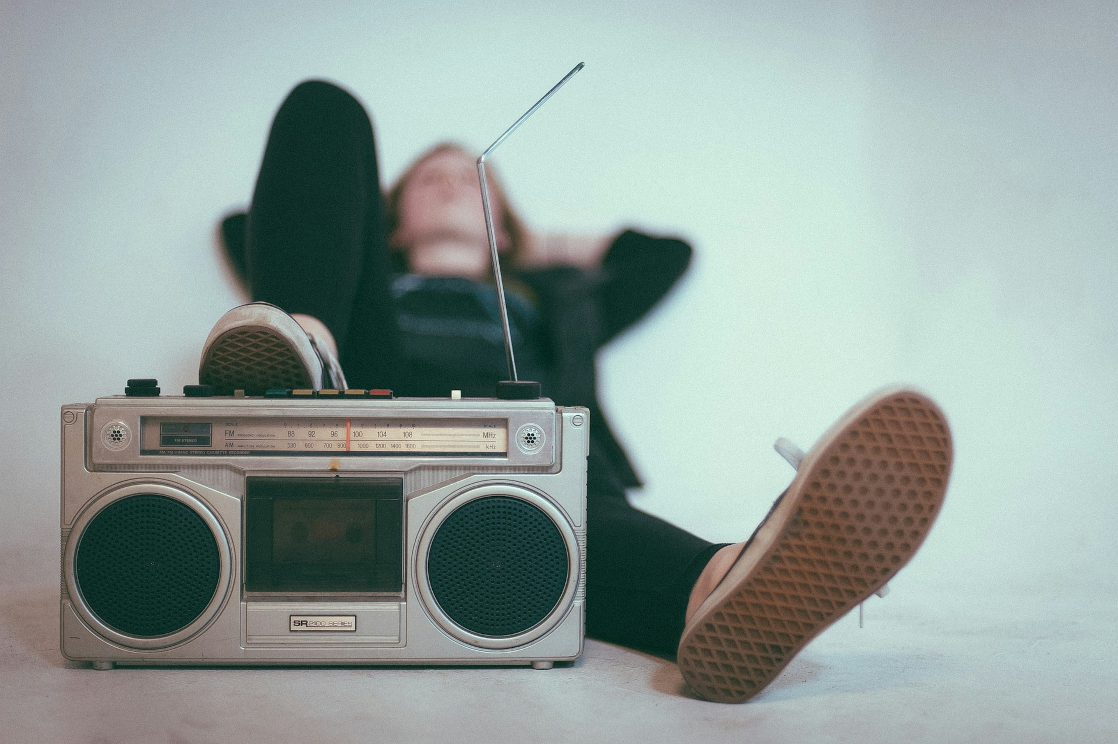 Person lehnt an Wand und stützt Fuß auf ein altes Radio.