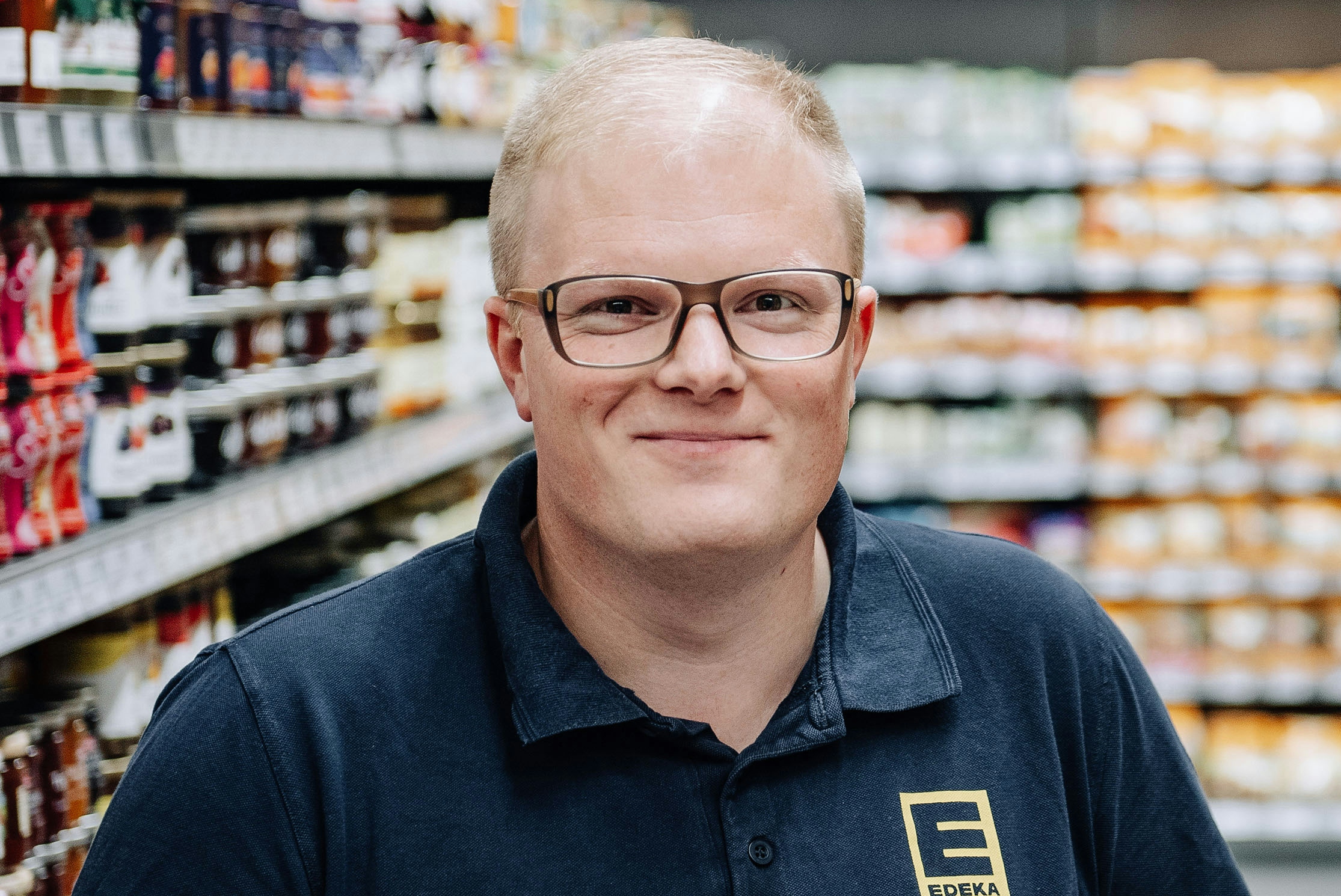 Benedikt Paul stands smiling in front of a shelf of goods