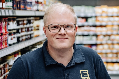 Benedikt Paul stands smiling in front of a shelf of goods
