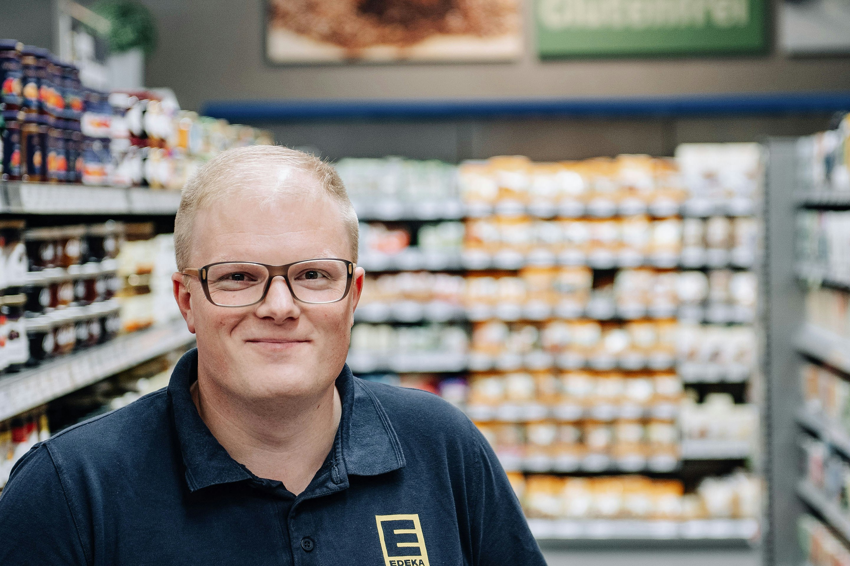 Benedikt Paul steht lächelnd vor einem Supermarktregal