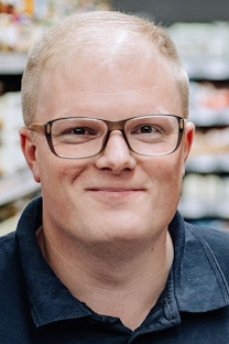 Benedikt Paul stands smiling in front of a food shelf