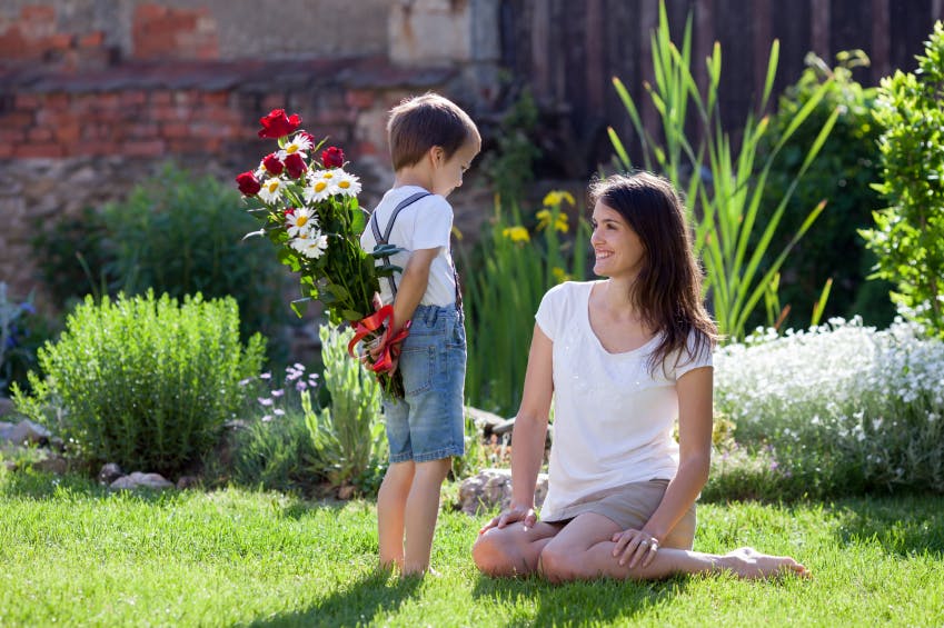 Un niño sorprende a su madre con un ramo de flores por su cumpleaños. 