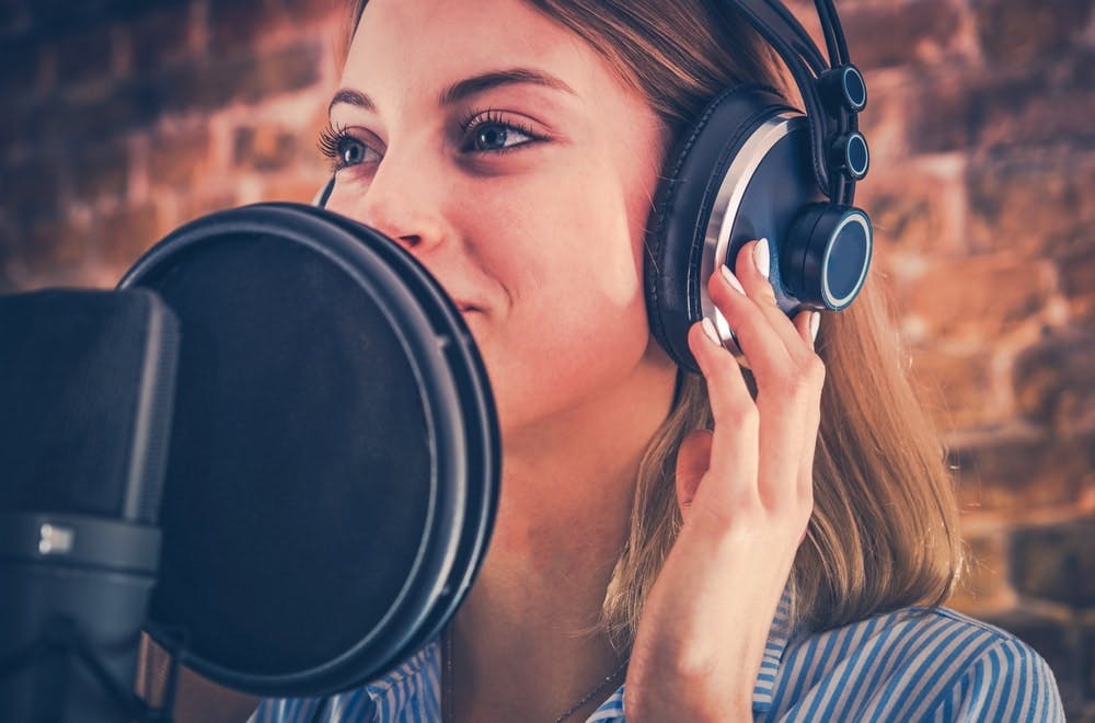 Una mujer cantando con cascos y delante de micro en un estudio de grabación profesional