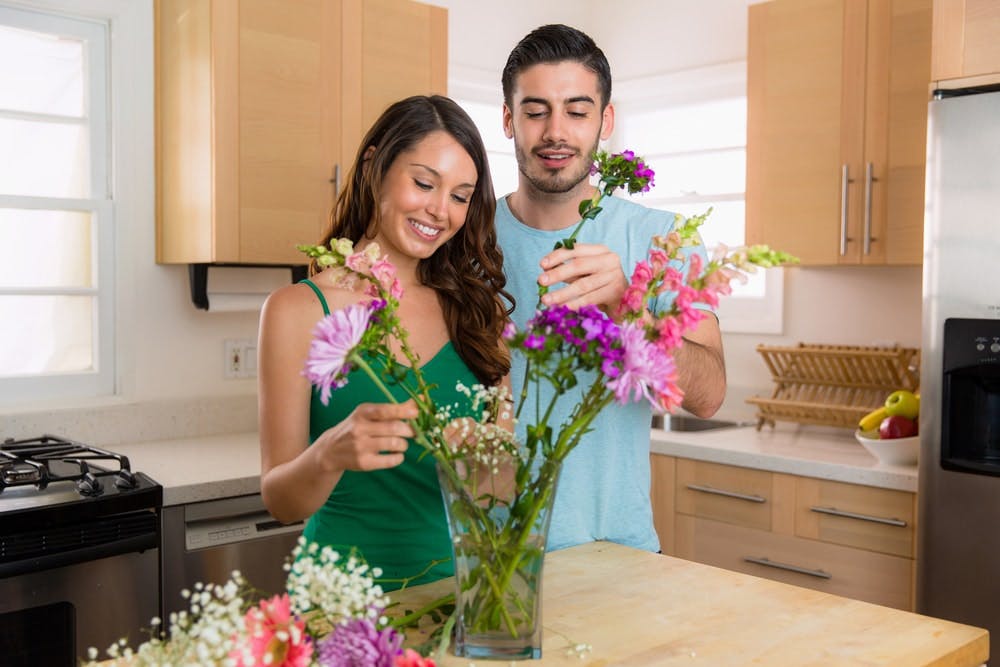 Una pareja arregla un ramo de flores en un jarrón en su cocina