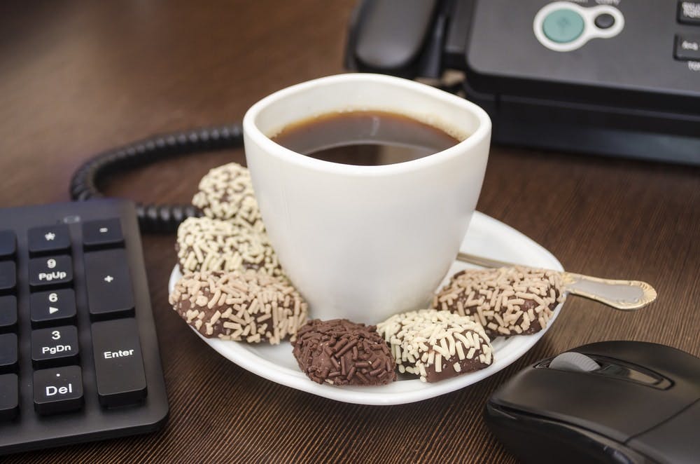 Una taza de café con bombones de chocolate en una mesa de oficina