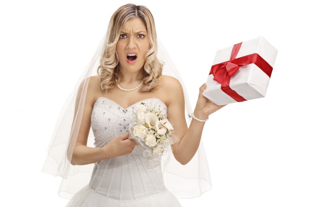 Young displeased bride holding a small wedding present isolated on white background