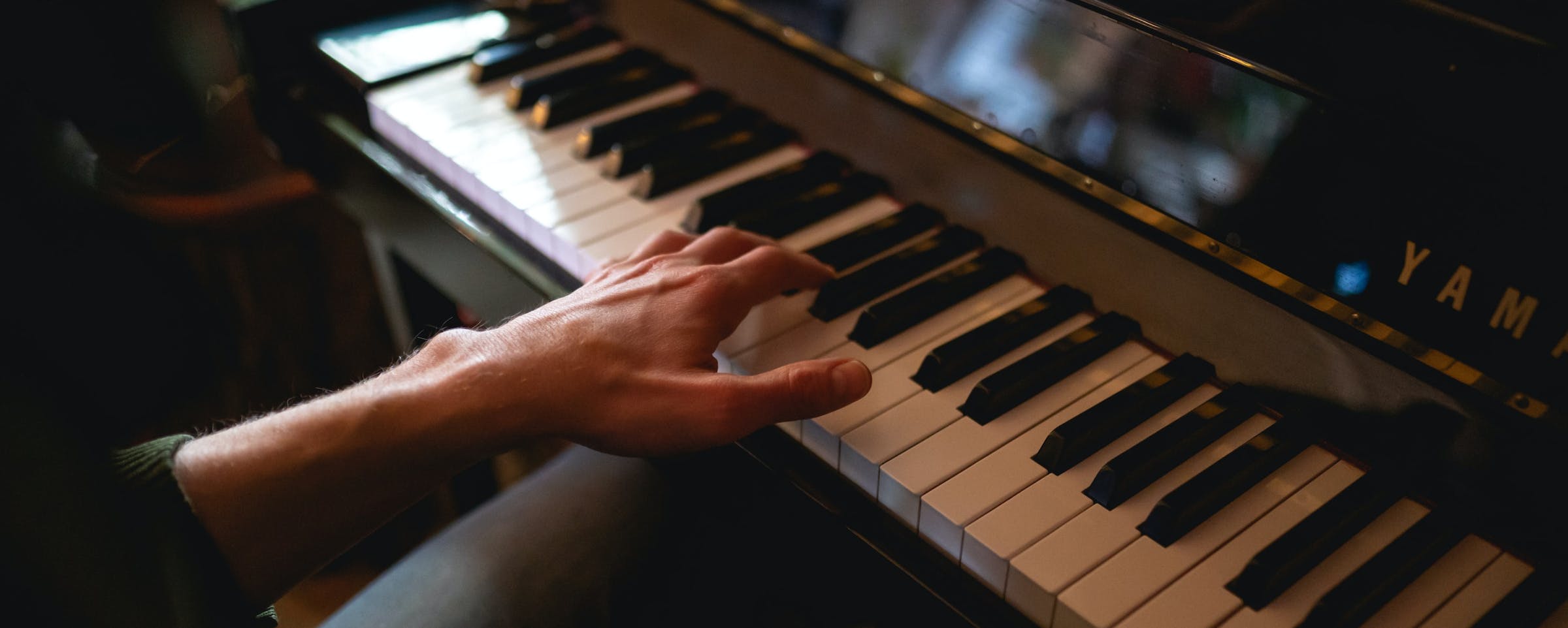 A left hand plays on an old Yamaha piano 