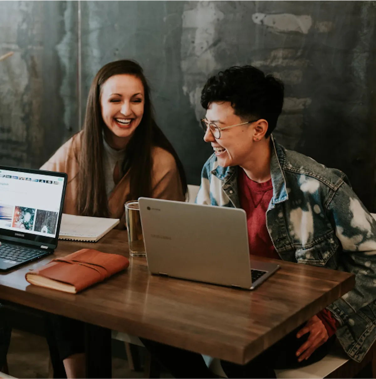 two workers laughing in front of laptops