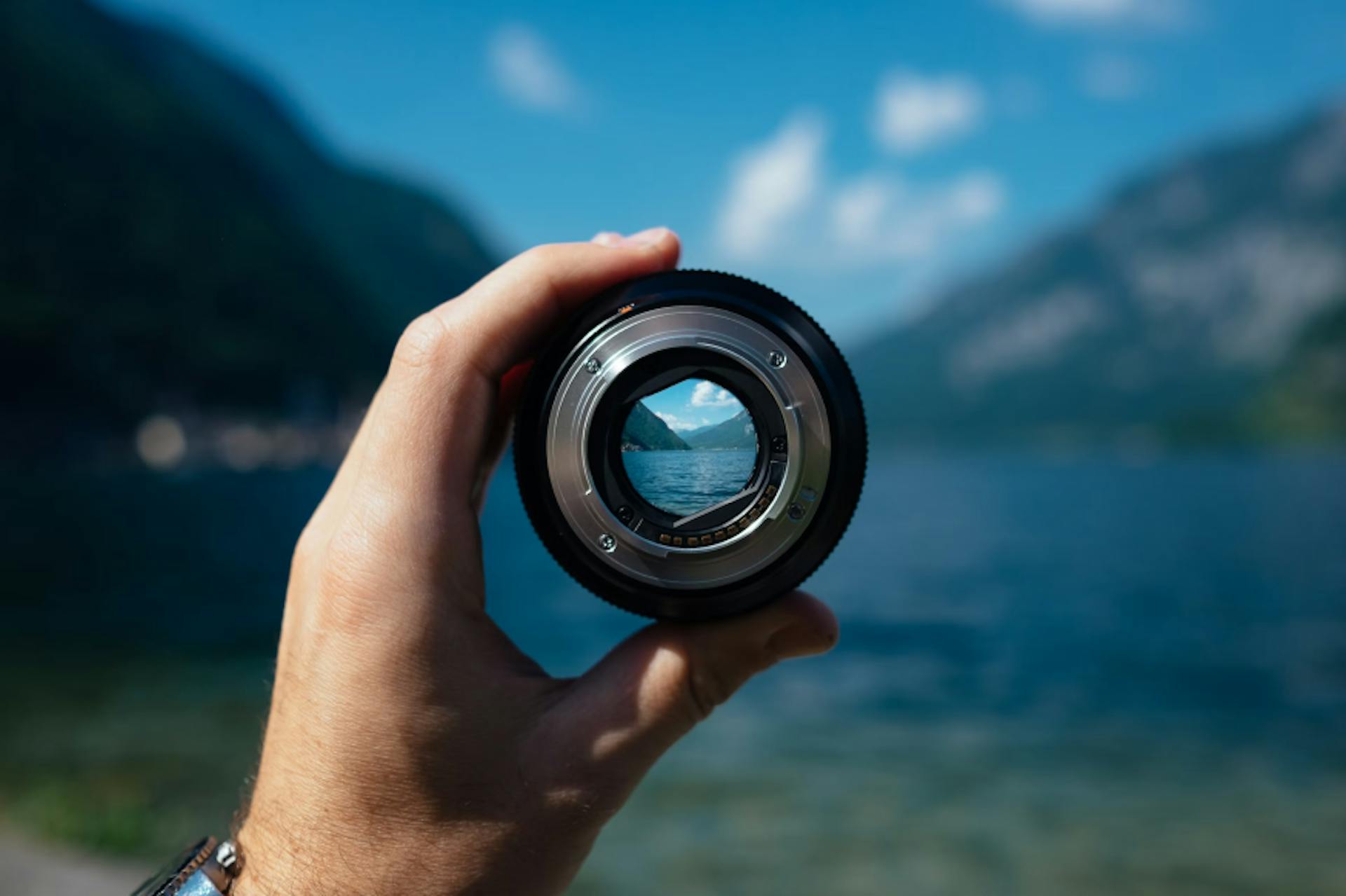 A camera lens held in front of mountains, demonstrating focus