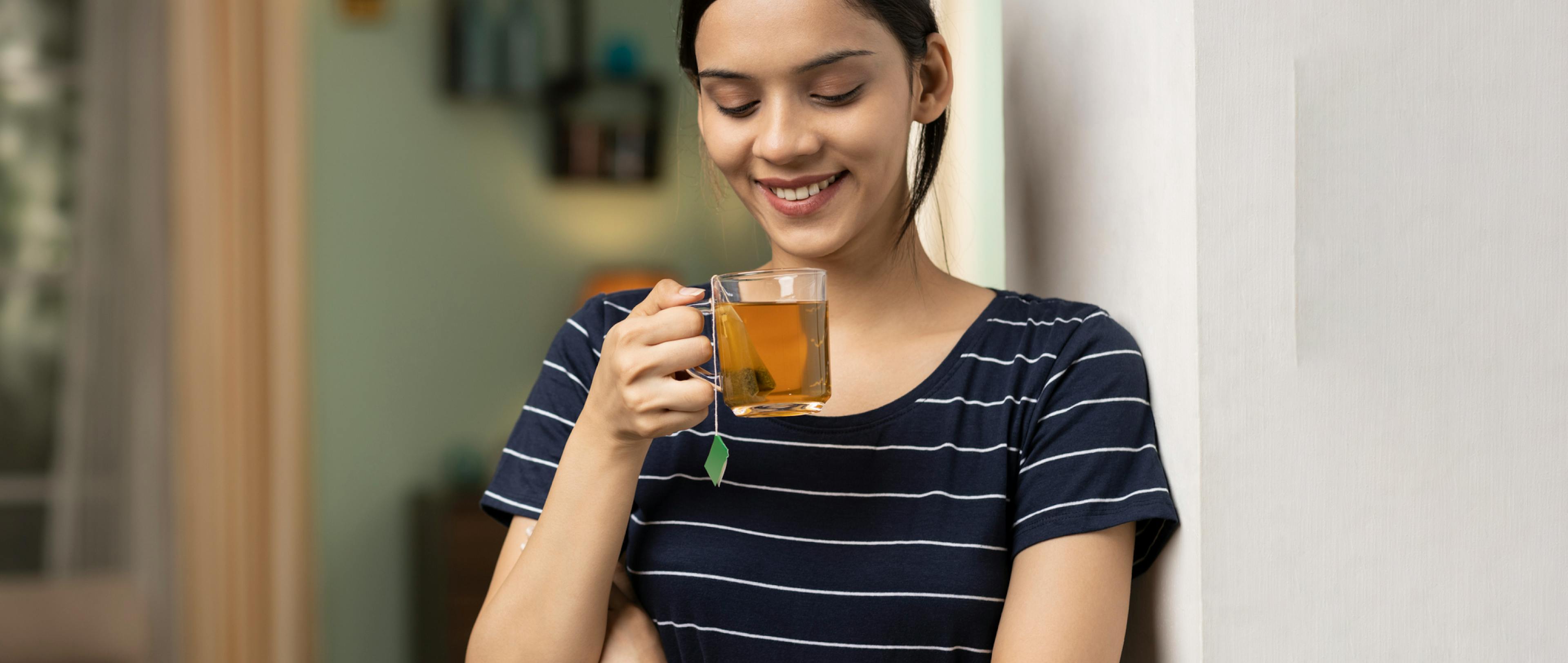 A smiling woman holding a cup of green tea. 