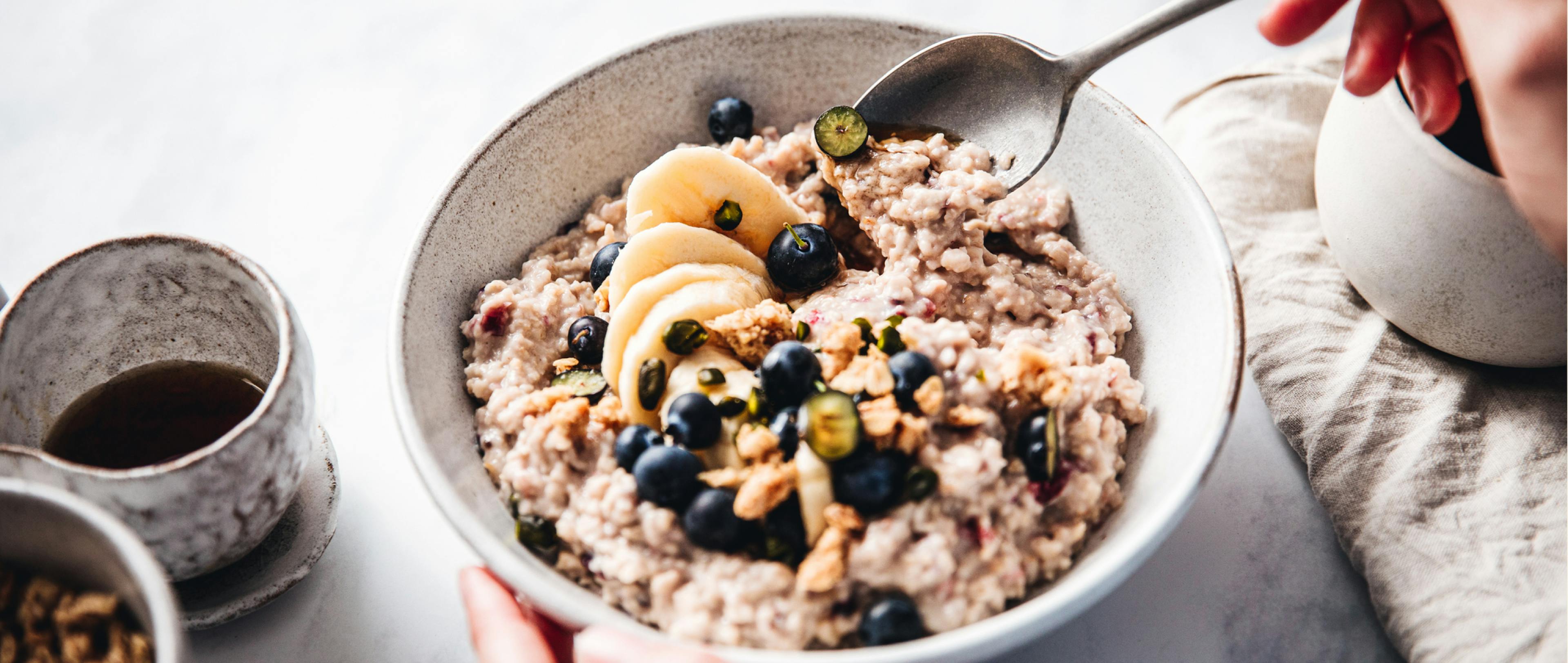 Close-up of a woman mixing oats flour, banana and blueberries in a bowl.