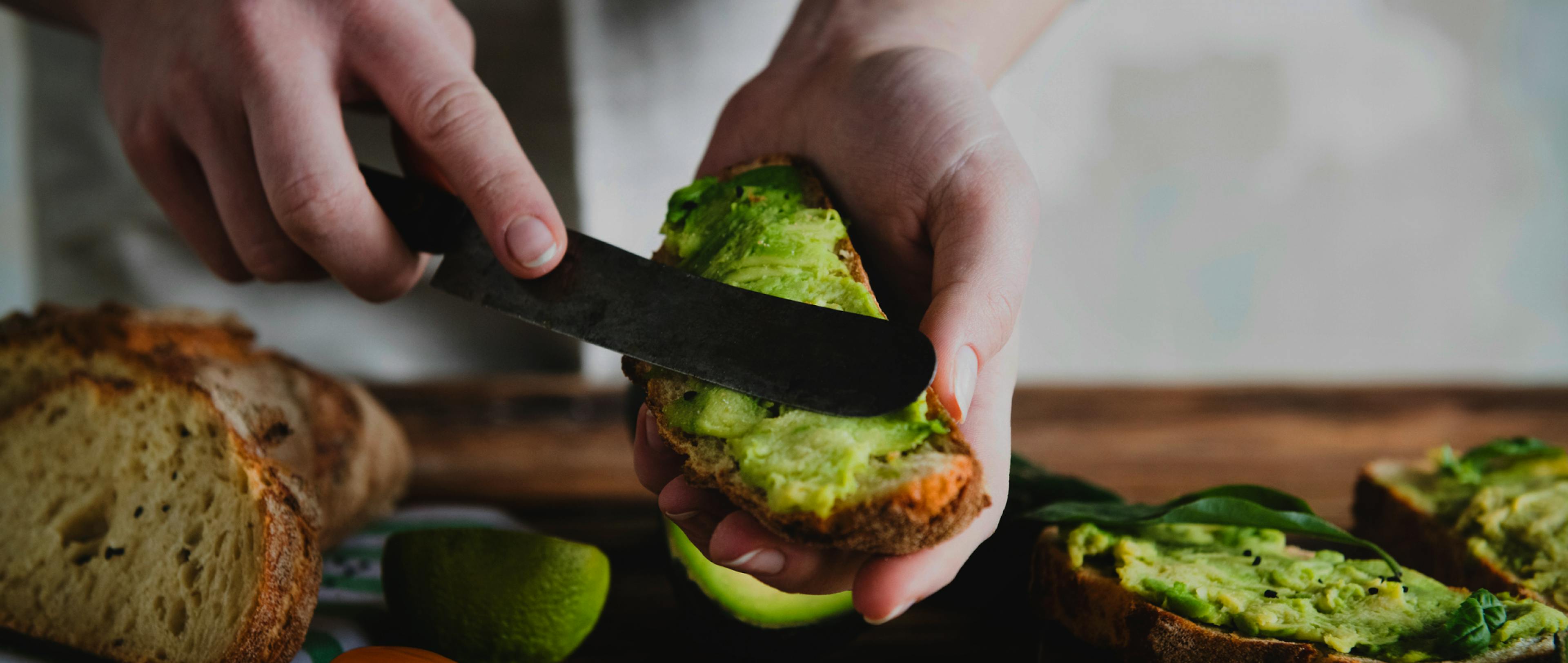 A guy applying avocado on bread with a knife. 