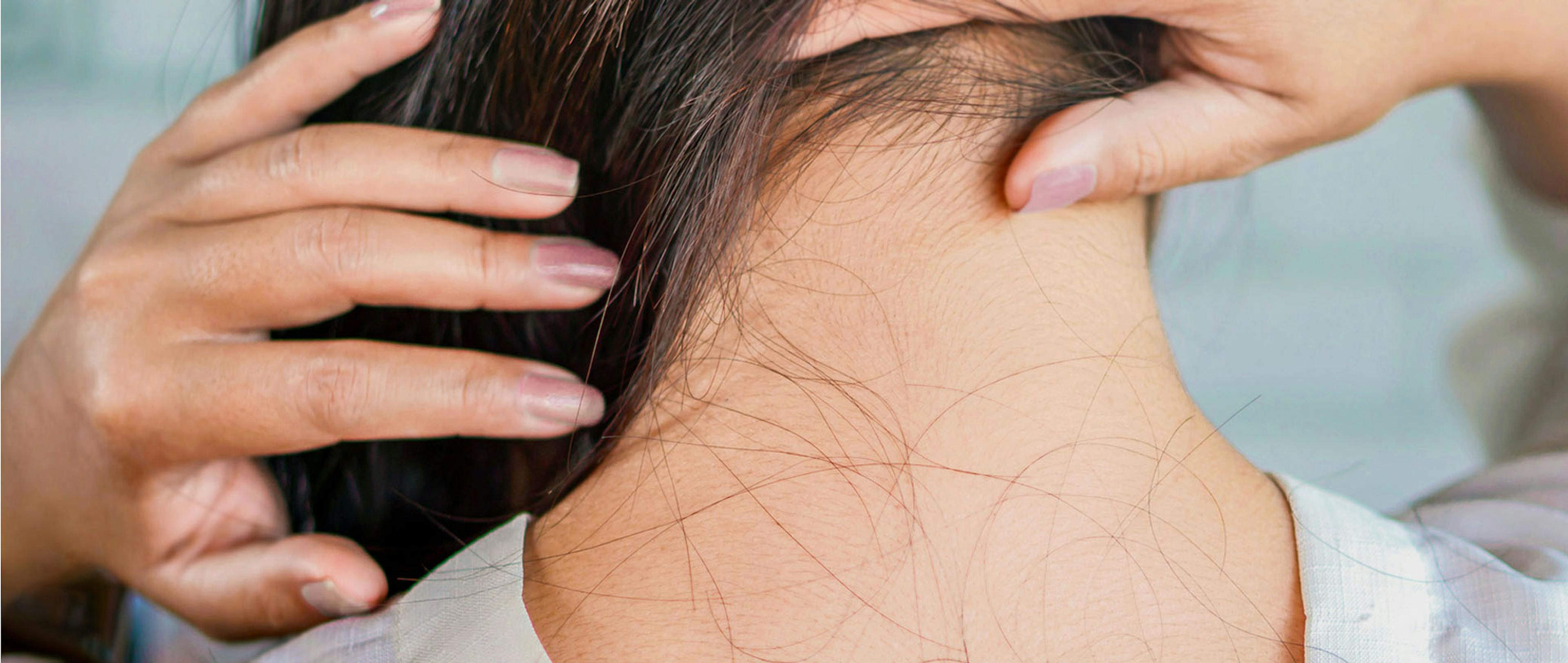 A close-up of a woman’s neck; her hair is swept over her shoulder, revealing a few loose strands of fallen hair. 