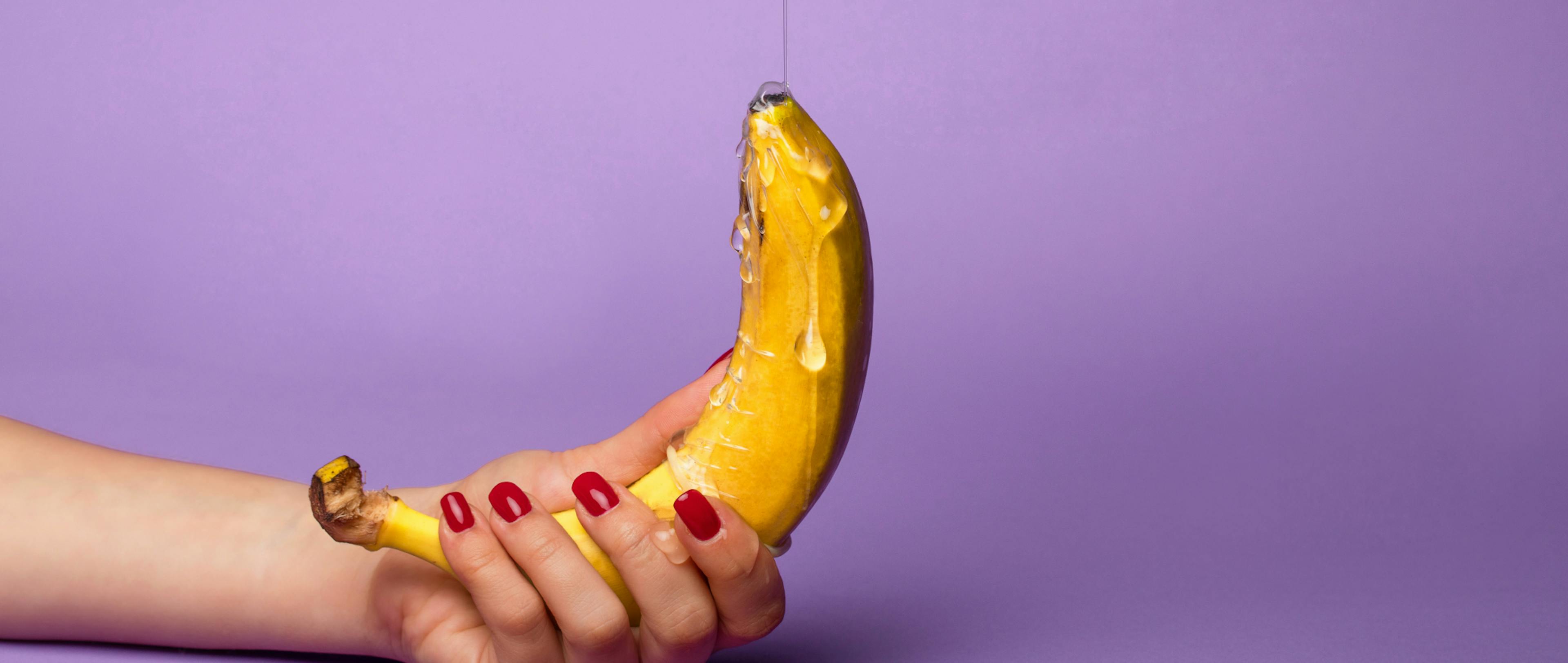 A woman holds the banana as lubricant falls on it.