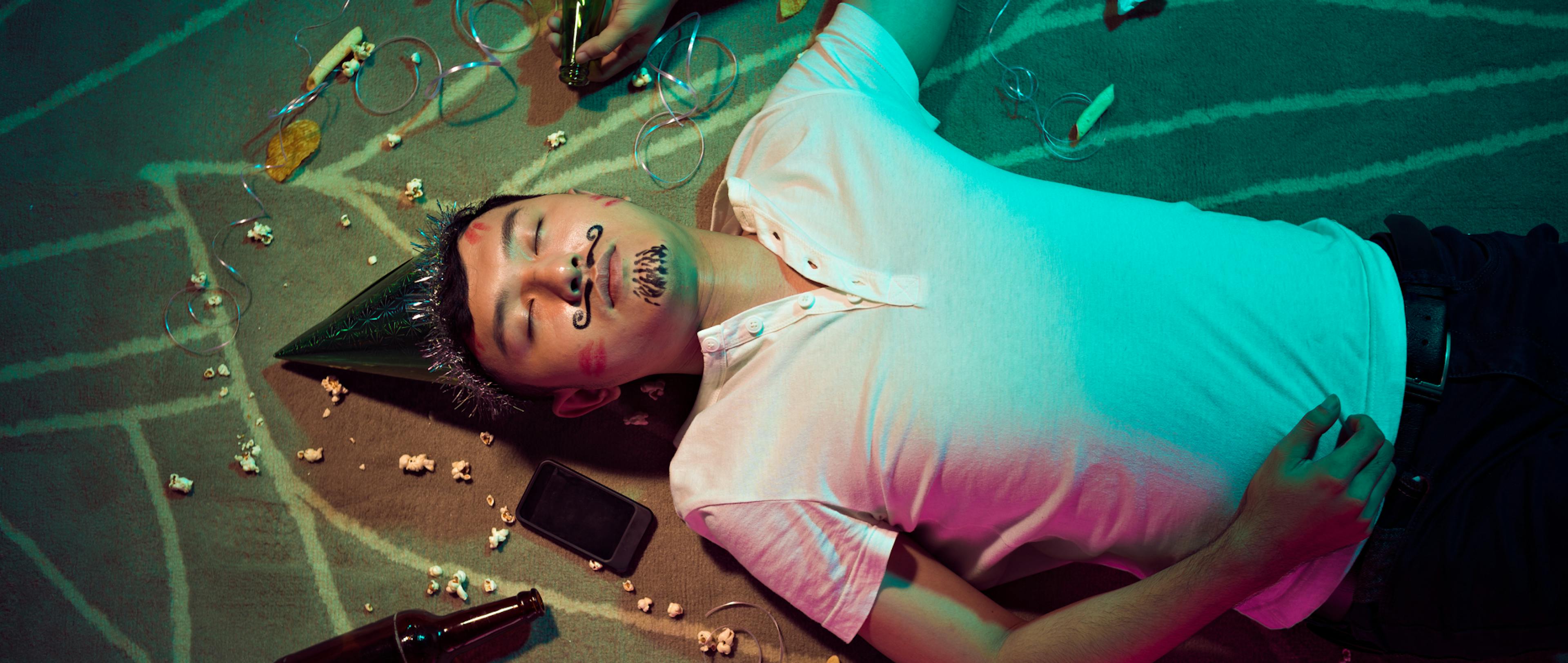 A drunk man lying on the ground after a party with bottles lying around.