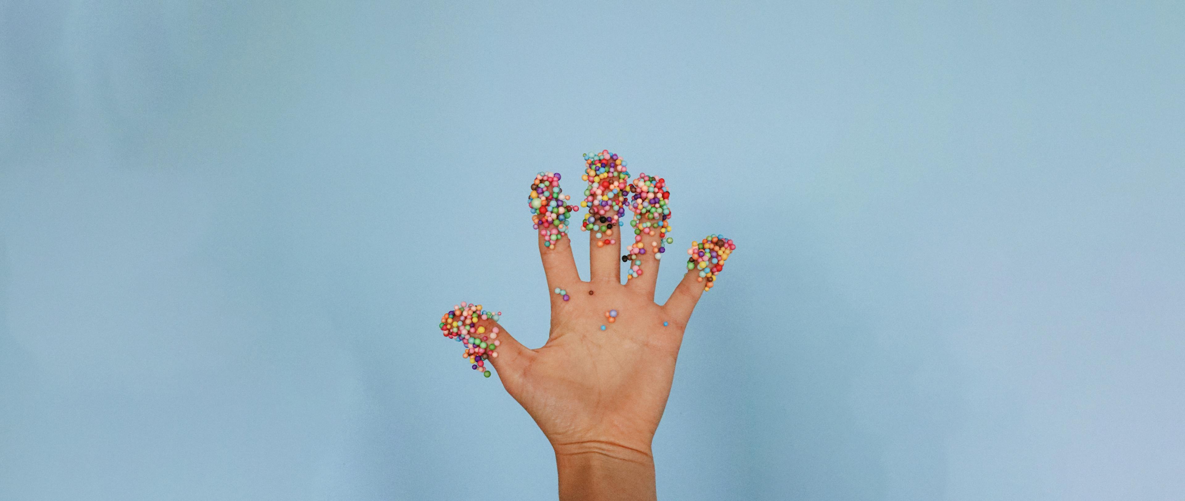 A person's hand with a lot of sprinkles on the fingertips. 