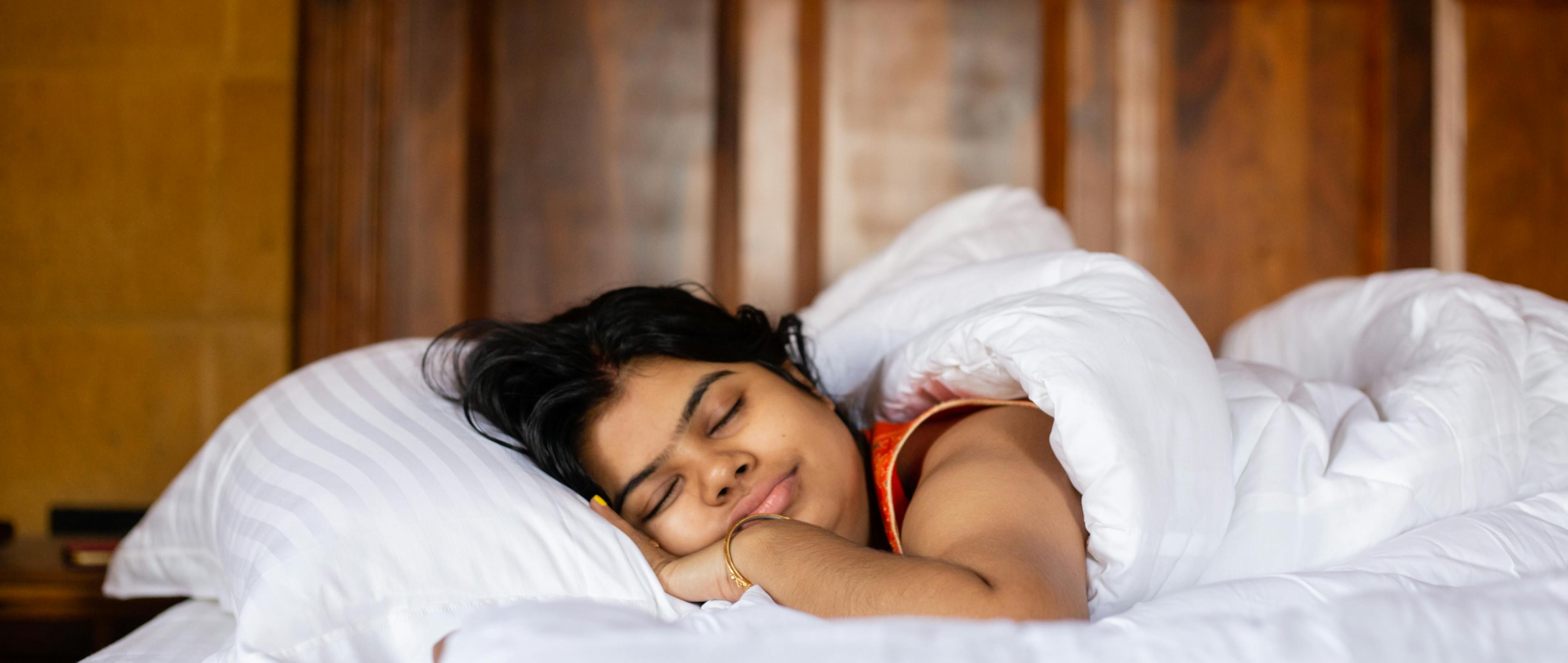 A young Indian pretty woman sleeping peacefully on a cozy white bed and pillow covering blanket with smiling face.