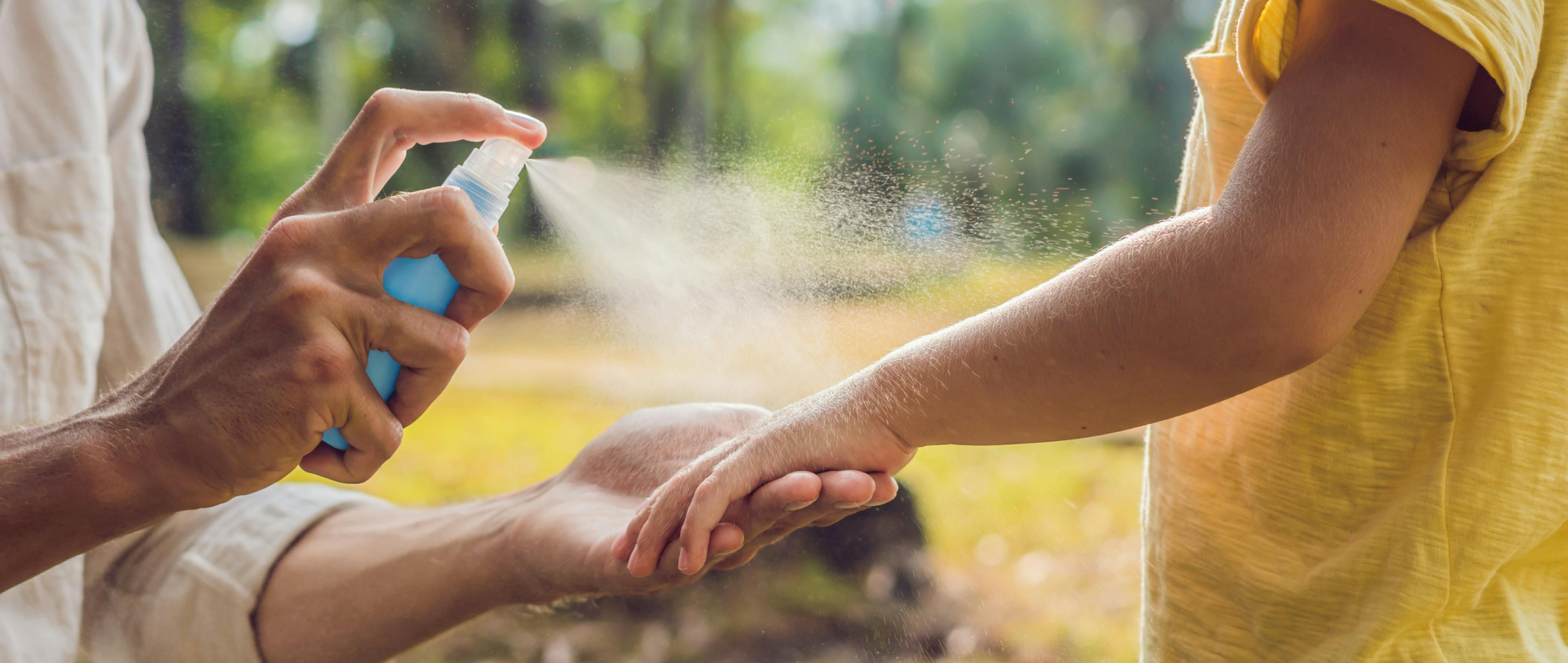 A father sprays insect repellent on his child's skin.