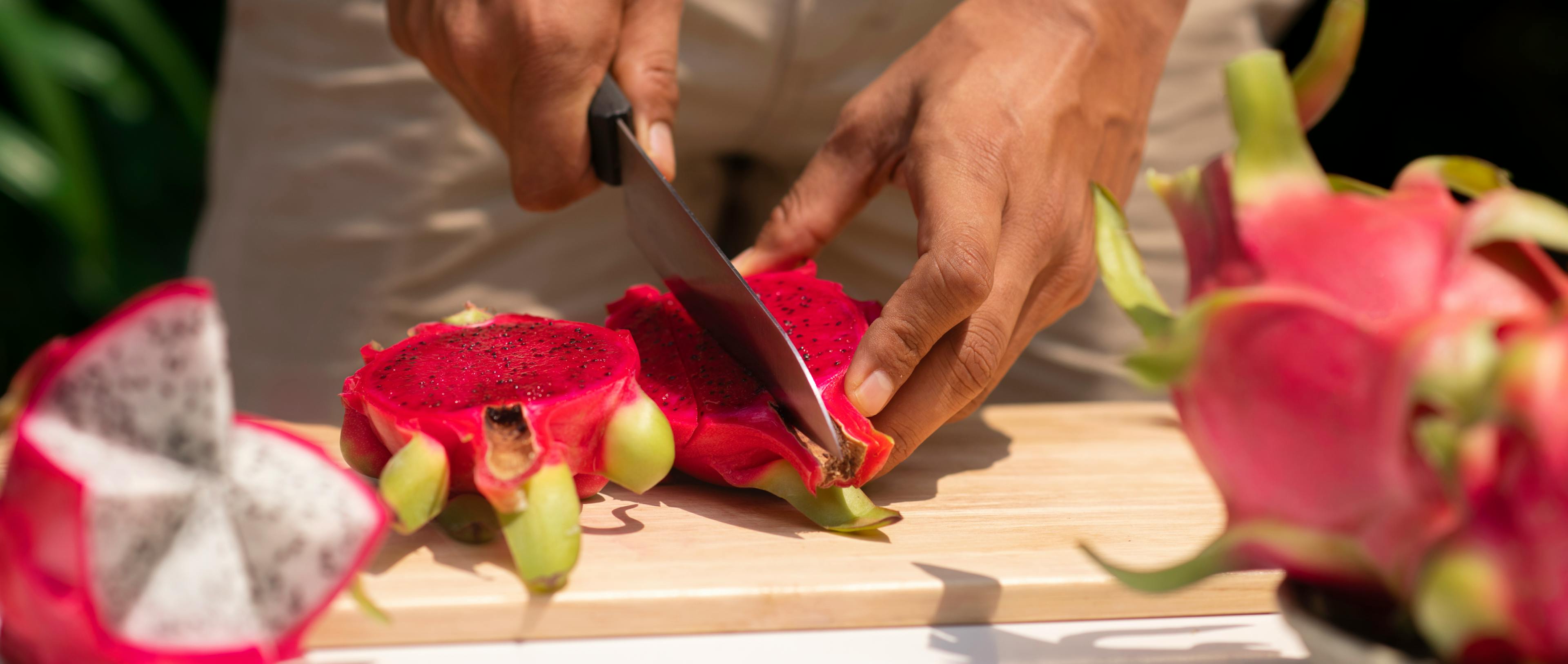 A man cutting dragon fruit with a knife on a table.