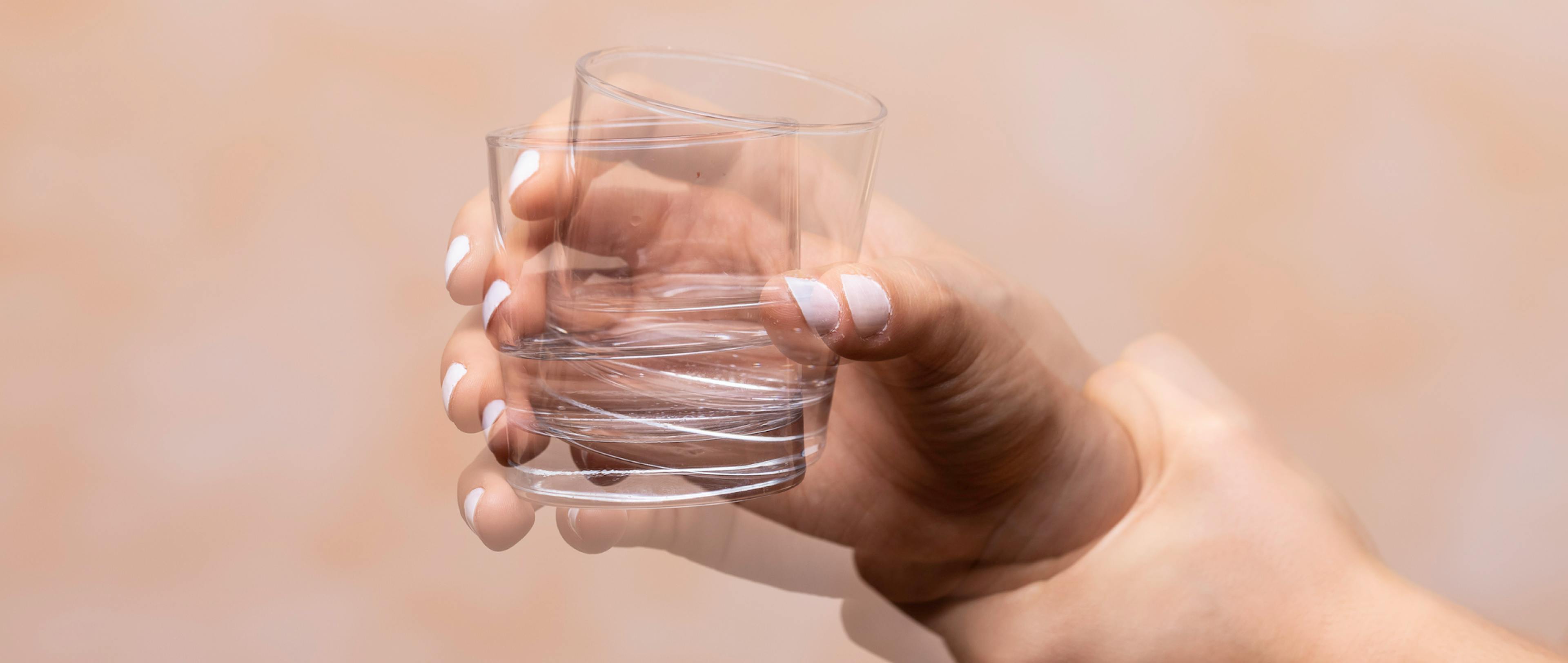 Closeup view on the shaking hand of a person holding drinking glass suffering from Parkinson's disease.