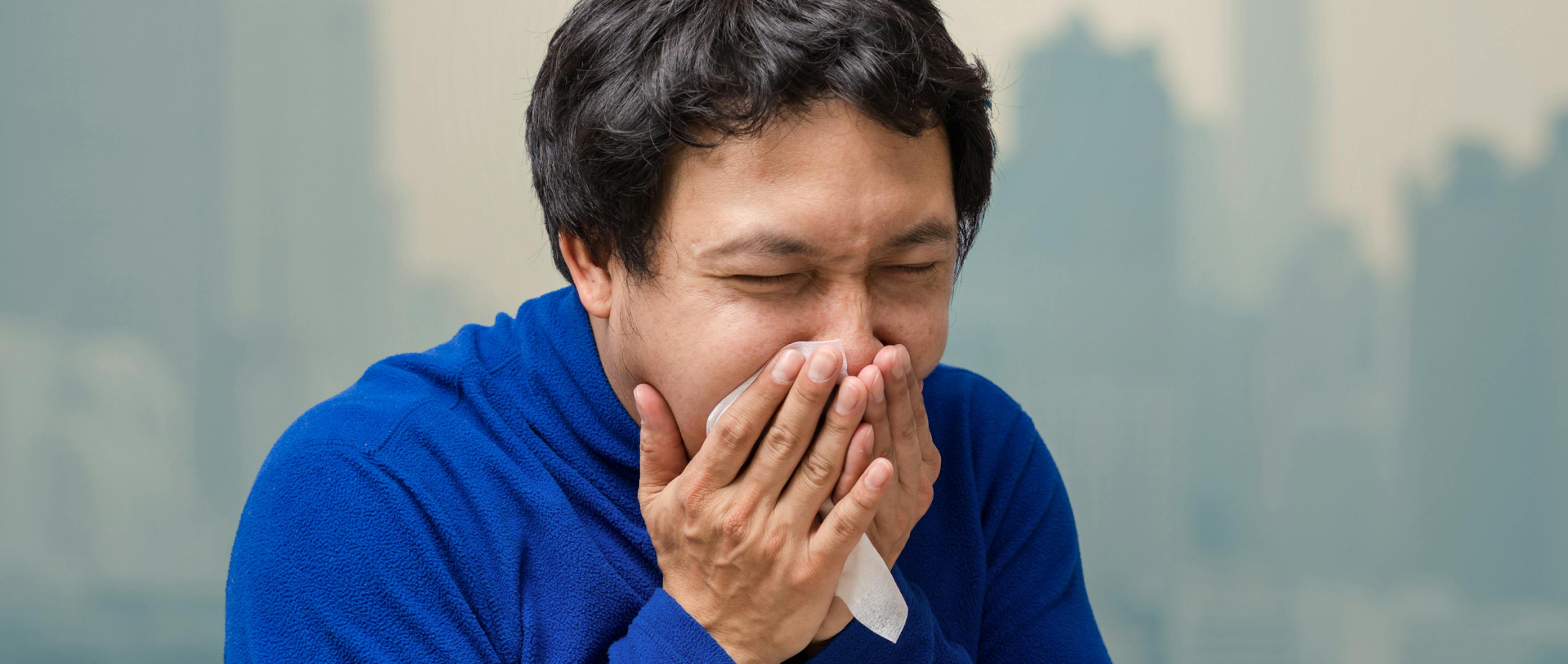 Asian man wearing the face mask against air pollution at the balcony of High Apartment which can see pollution and heavy fog over the Bangkok cityscape background.