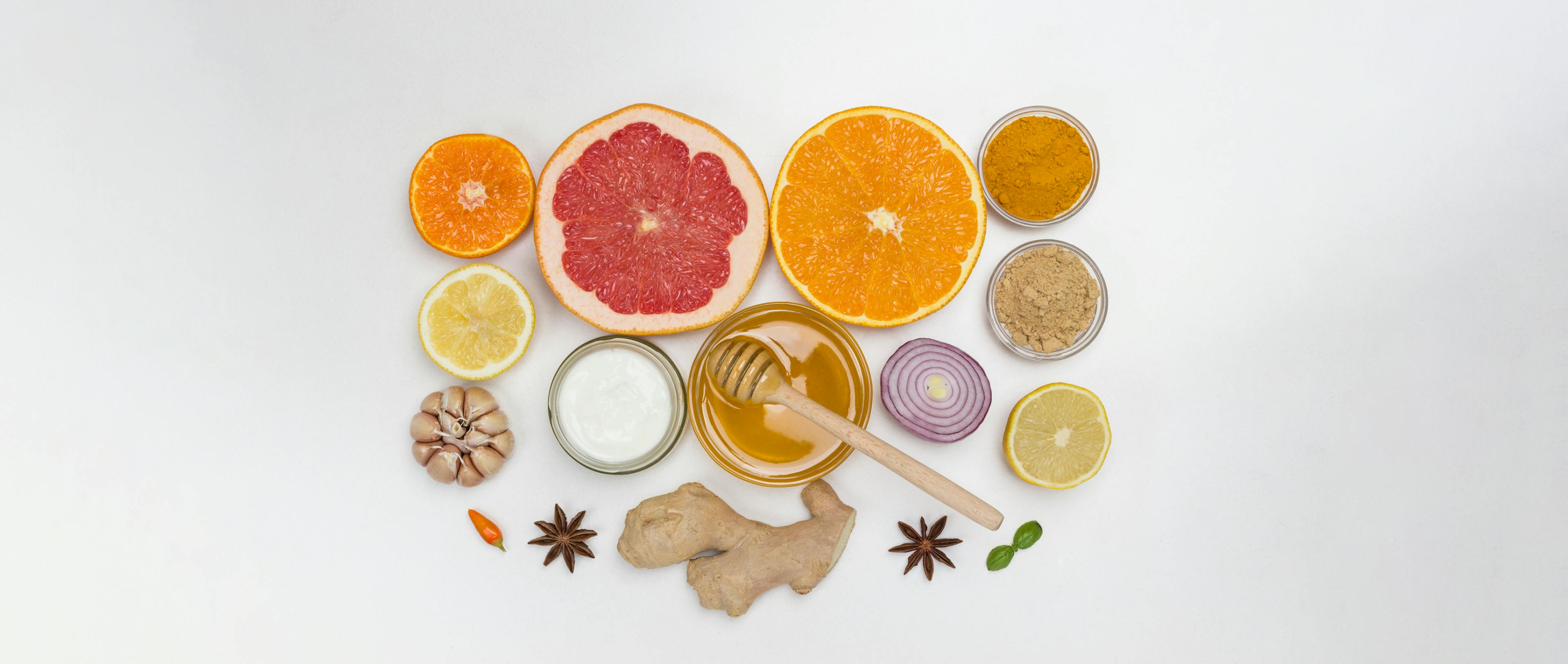 A flat lay of immunity-boosting foods featuring citrus fruits, whole spices, ginger, garlic, onion, and honey