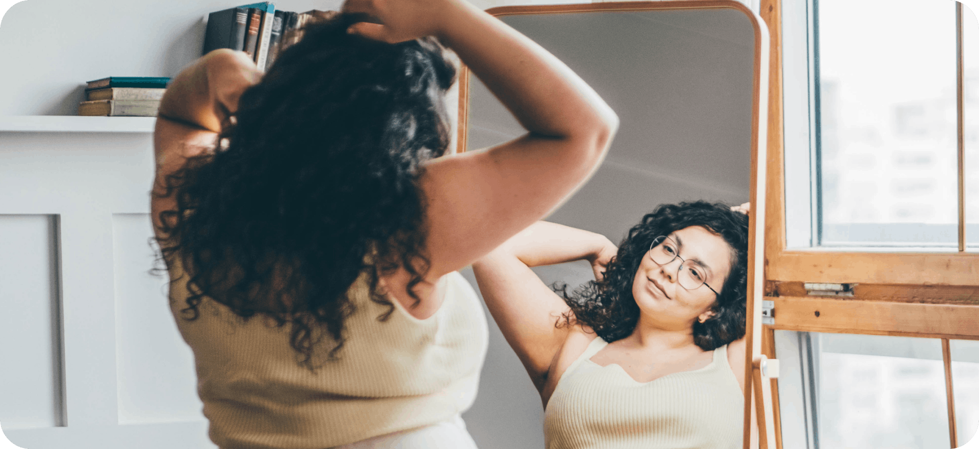 A woman stands before a mirror admiring herself. Caring for your appearance while undergoing the effects of cancer treatment on skin and hair is a sign of strength.
