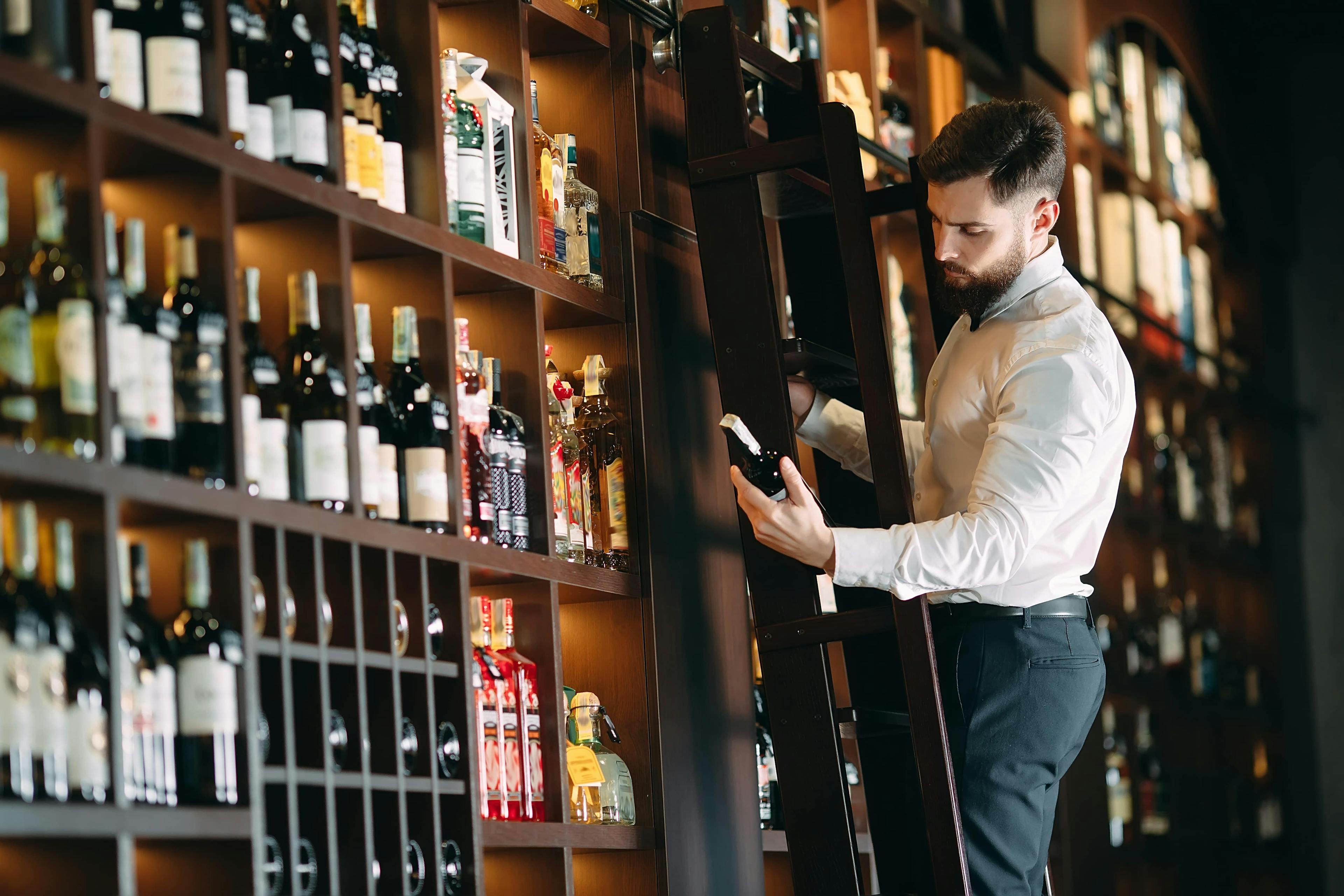 Man looking at some wine while on a ladder