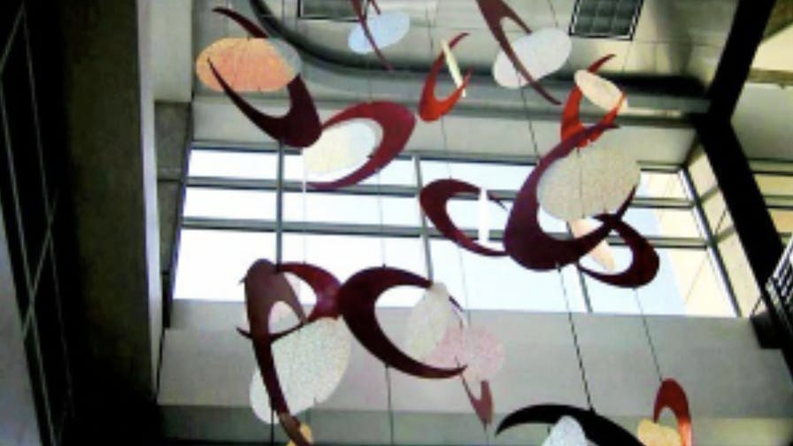 Hanging mobile sculpture with swirling red rings and speckled white ovals suspended in a tall glass atrium.