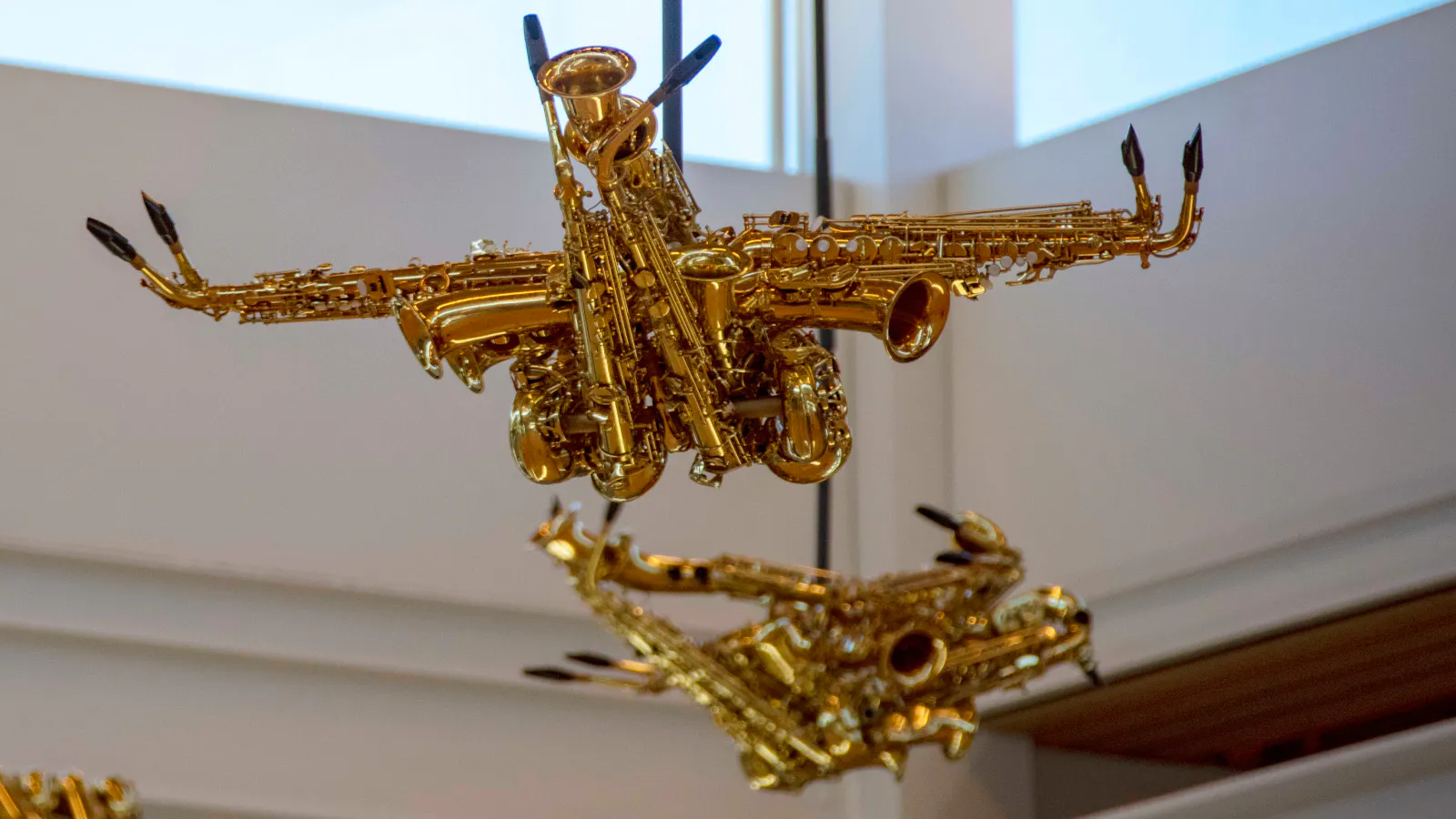 Close-up view of two suspended sculptures made from shiny brass instruments, primarily saxophones and trumpets, assembled to resemble birds or flying machines.