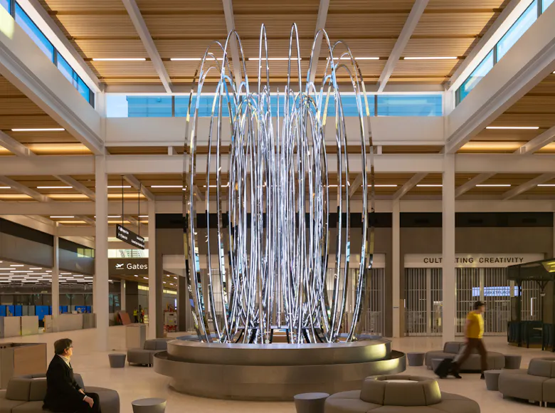 Tall, illuminated sculpture of looping metal rings in a bright Kansas City International Airport terminal seating area.