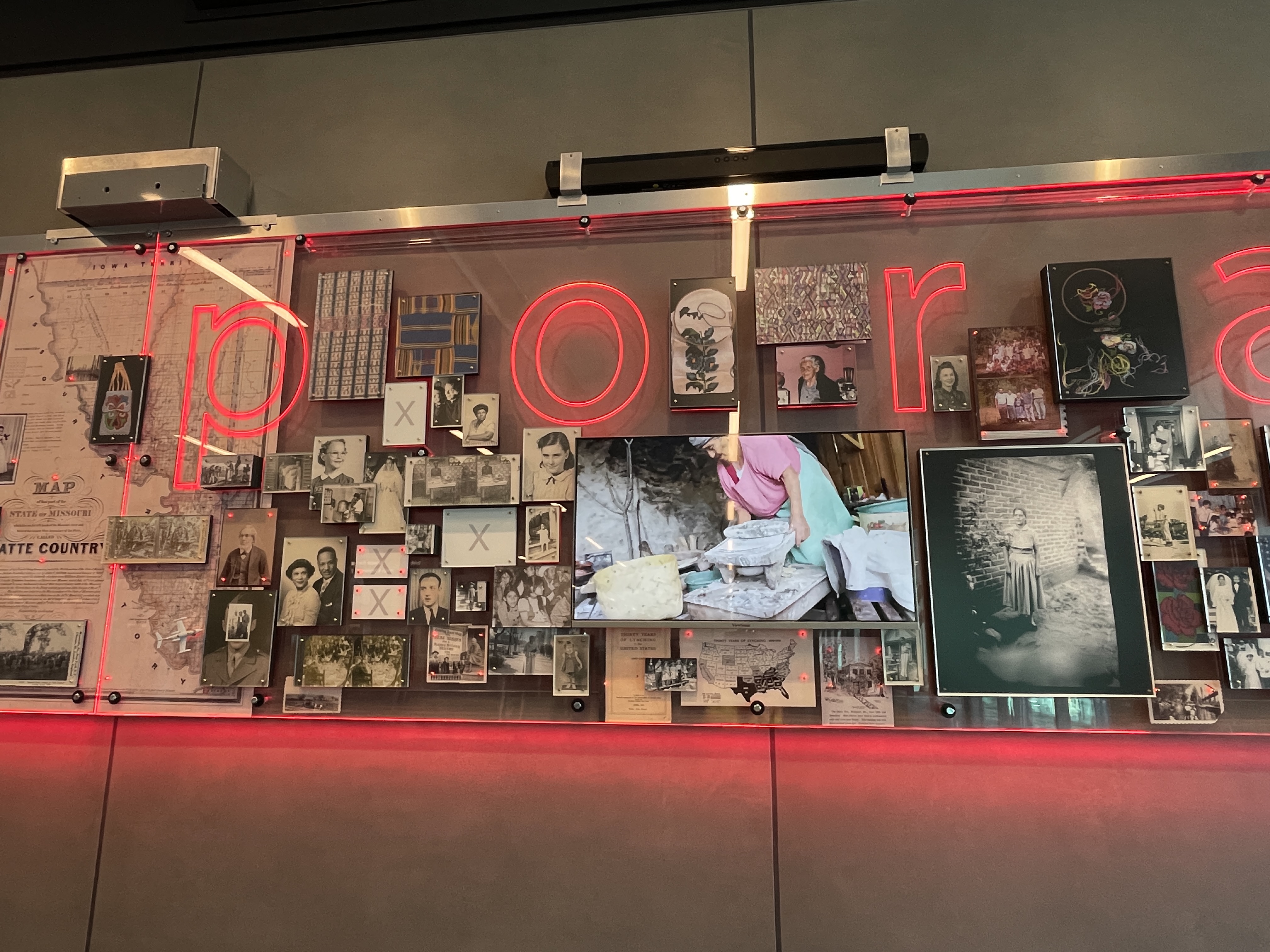 Right side of the “diasporia” installation, featuring vintage photographs, maps, and textiles layered behind red neon letters and a glass panel.