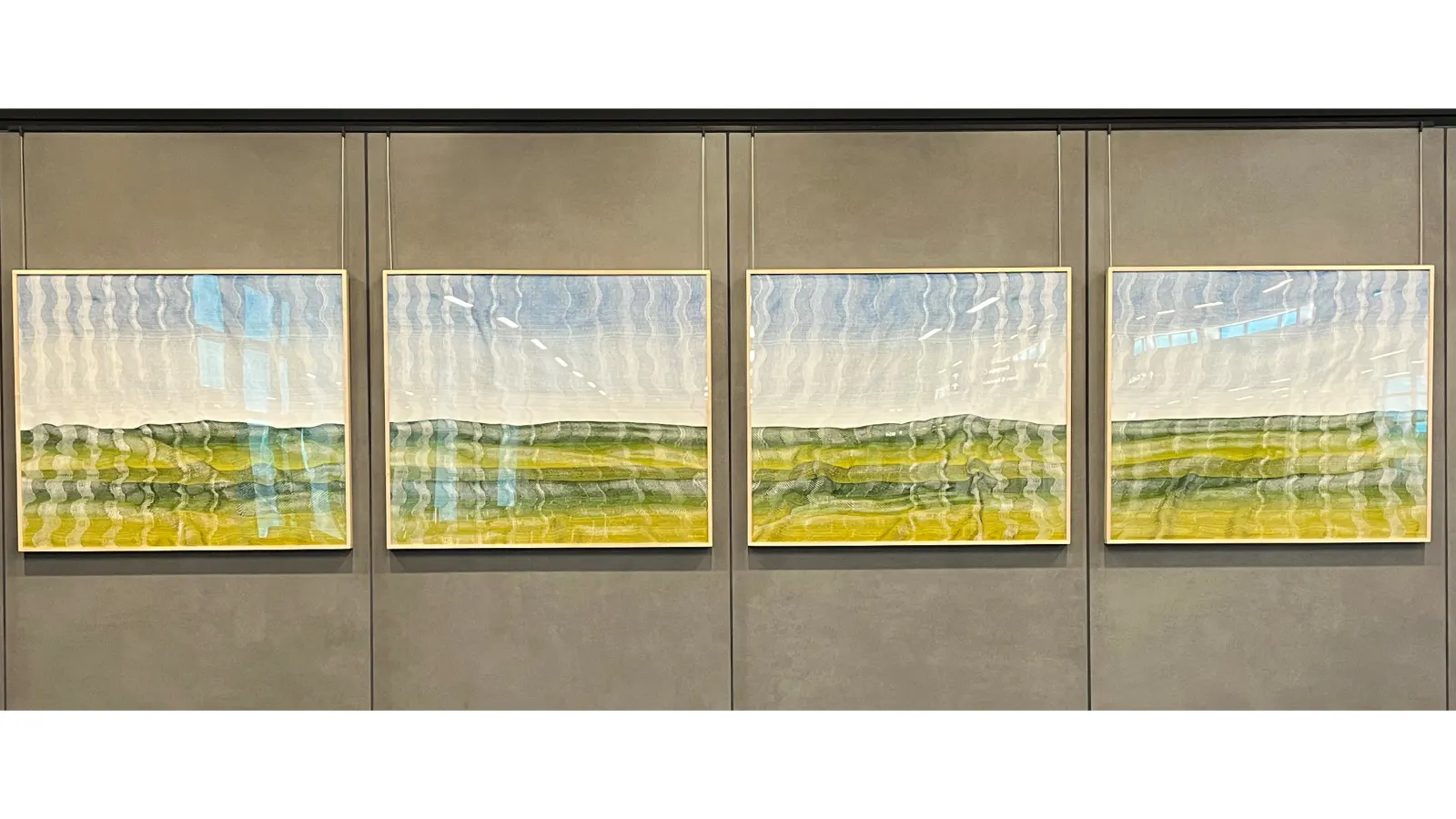 Four-panel landscape artwork featuring abstract horizontal bands of green, yellow, and blue tones, resembling rolling hills beneath a bright sky with a wavy, reflective texture.