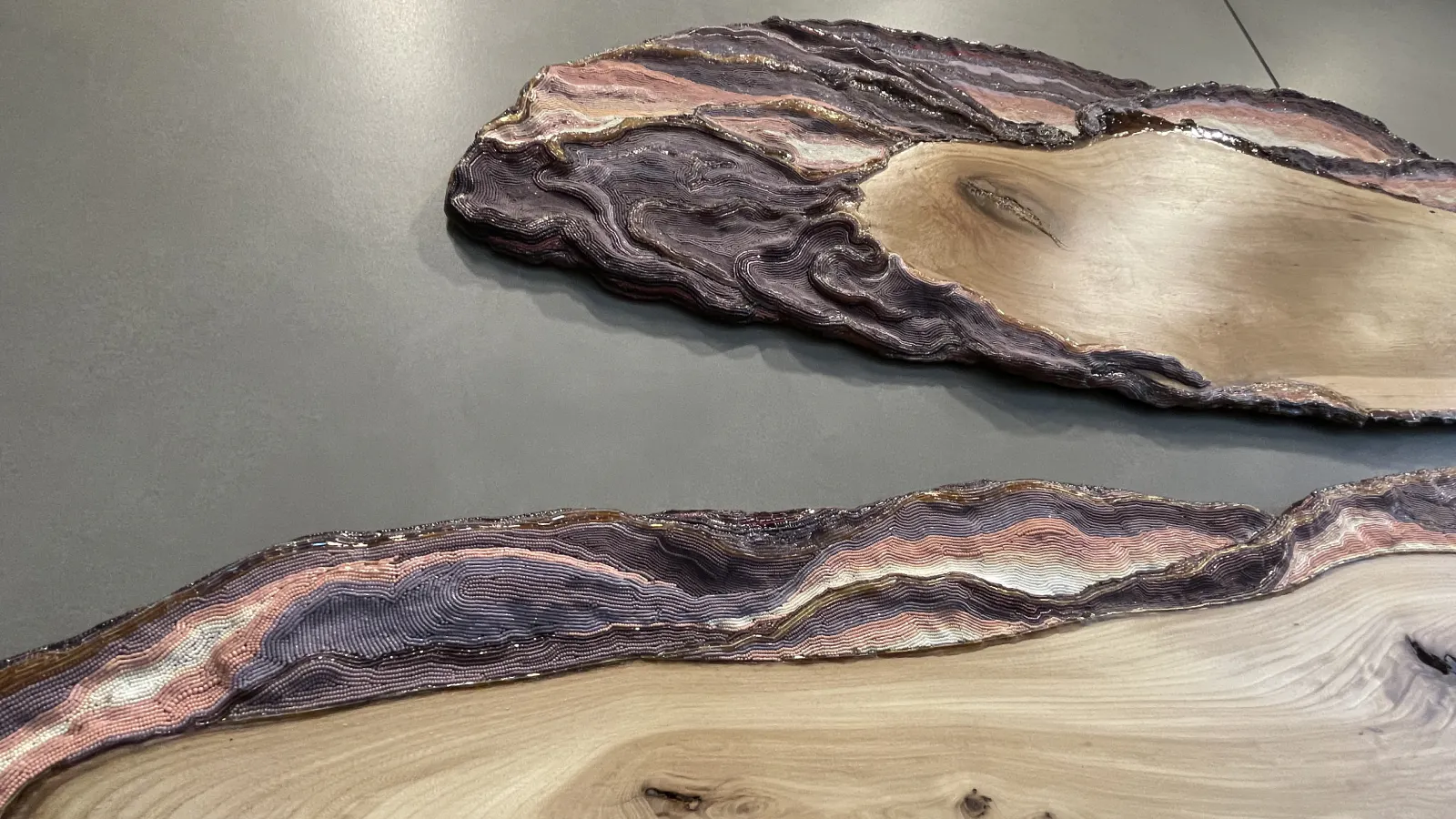 Close-up of sculptural slabs with swirling grain patterns and textured, layered purple and pink resin edges resembling topographic lines or geological formations.