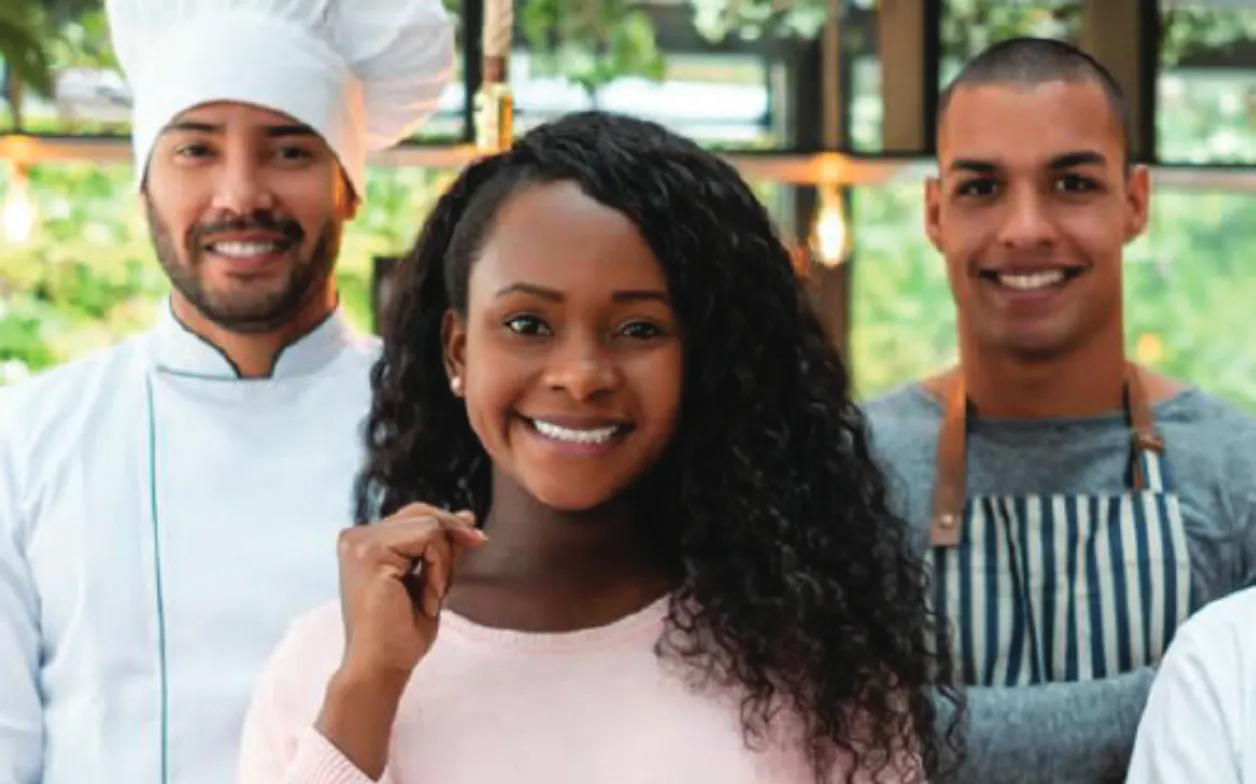 Three smiling individuals pose in a cafe setting.