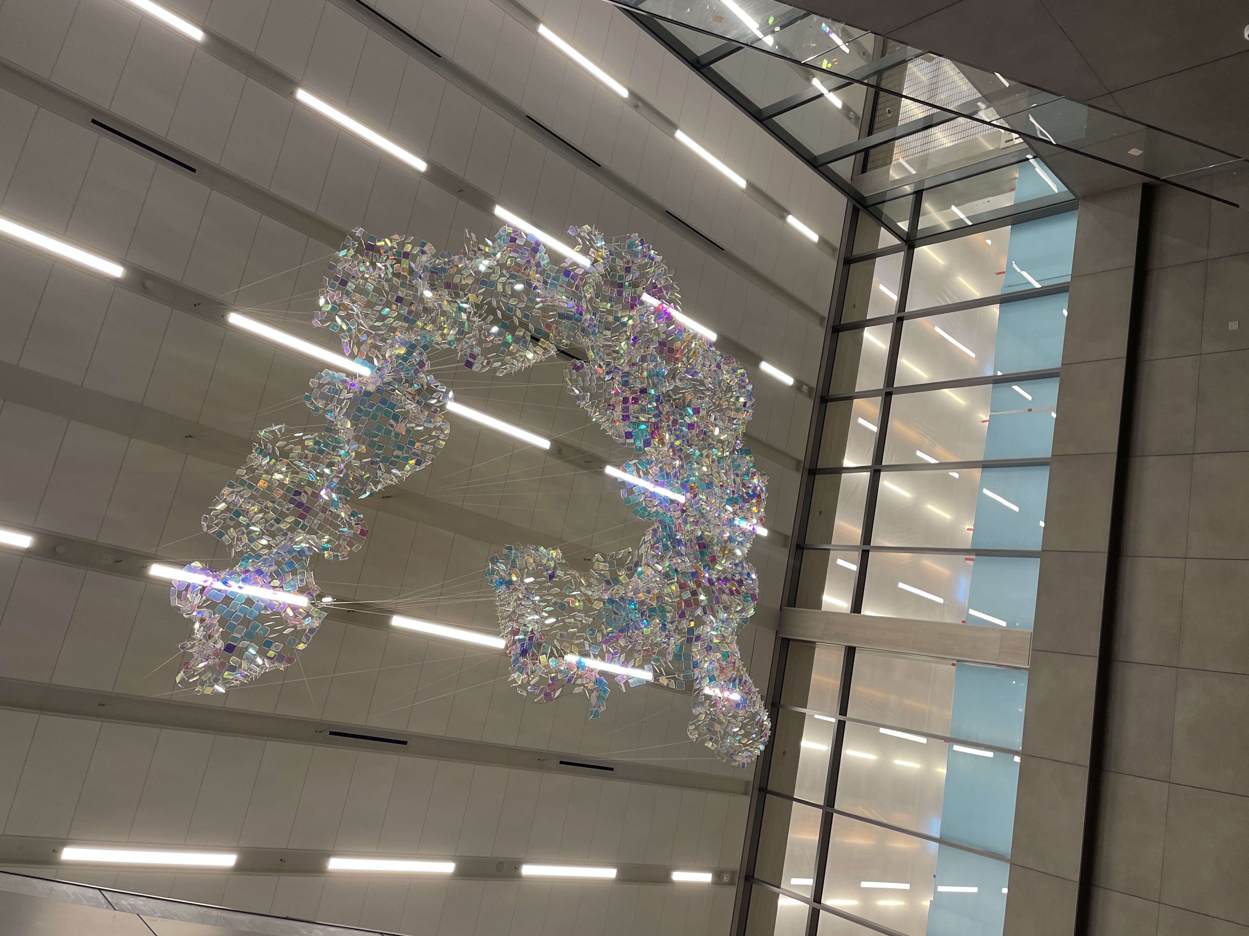 Ceiling-mounted sculpture of shimmering, iridescent mesh suspended with wires at Kansas City International Airport.