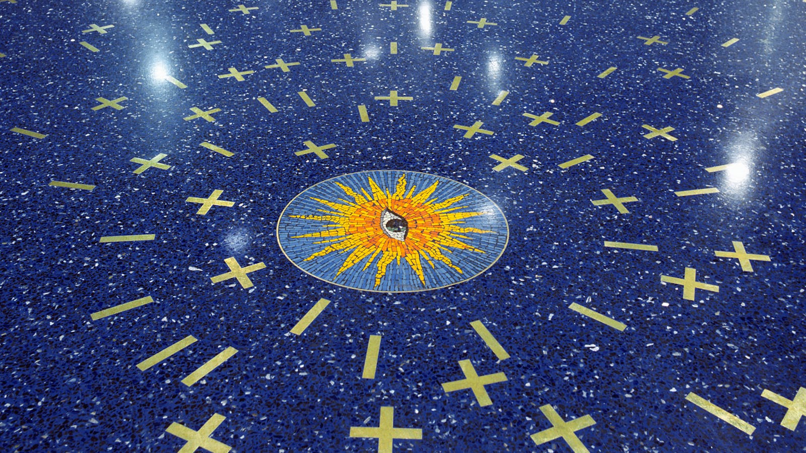 Mosaic artwork on a blue speckled airport floor at Kansas City International Airport, featuring a central sunburst design with surrounding gold X and line shapes.