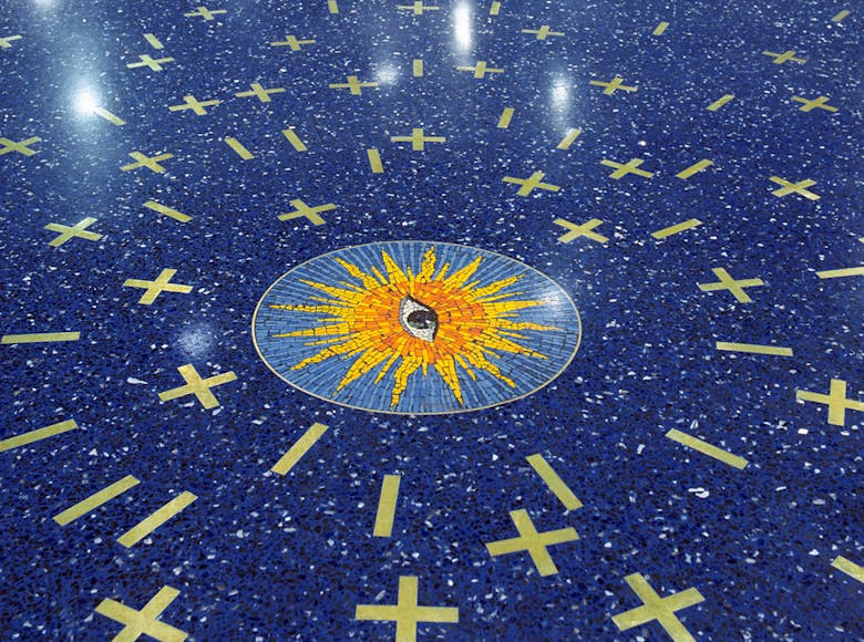 Mosaic artwork on a blue speckled airport floor at Kansas City International Airport, featuring a central sunburst design with surrounding gold X and line shapes.