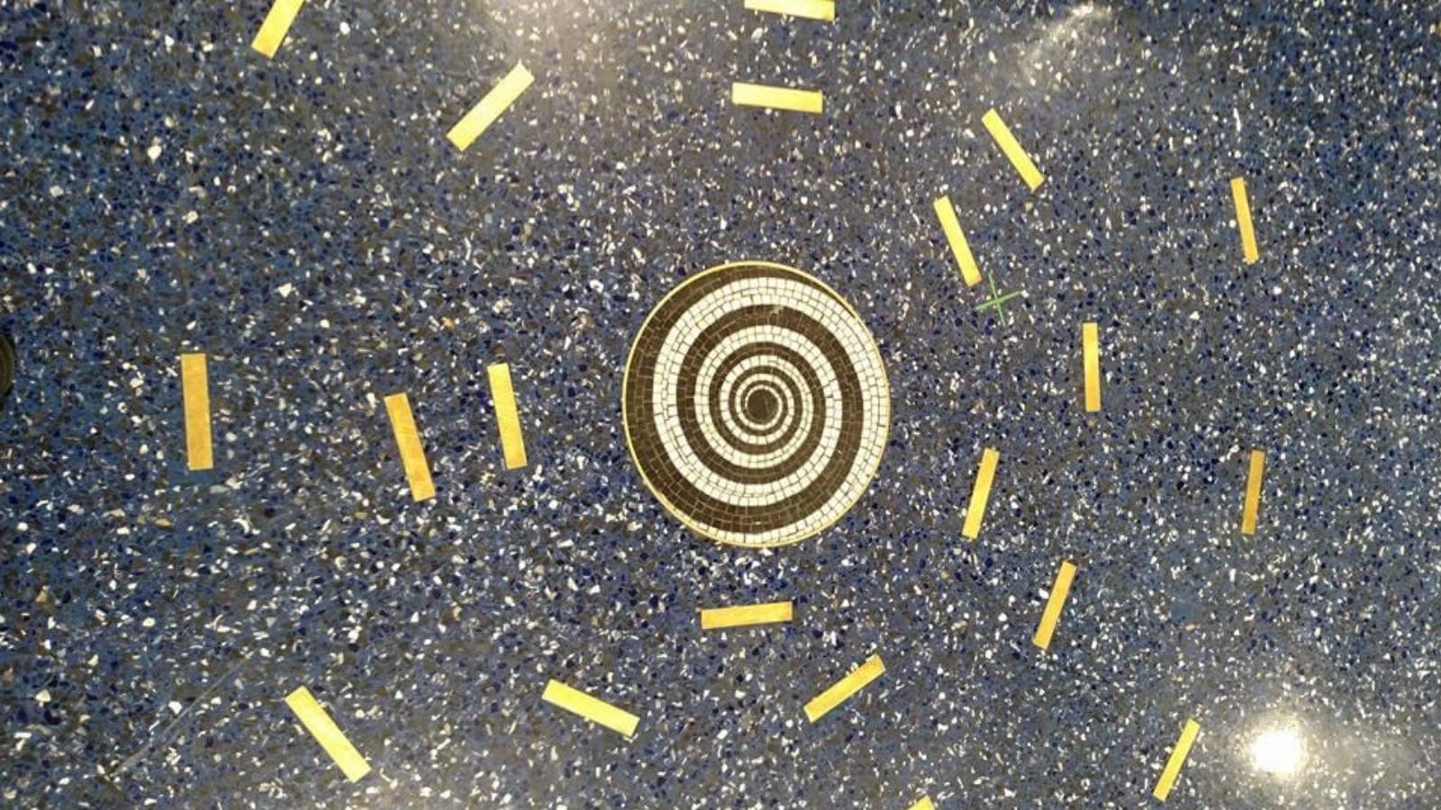 Spiral mosaic on a blue speckled floor at Kansas City International Airport, surrounded by short gold bars in a circular pattern.