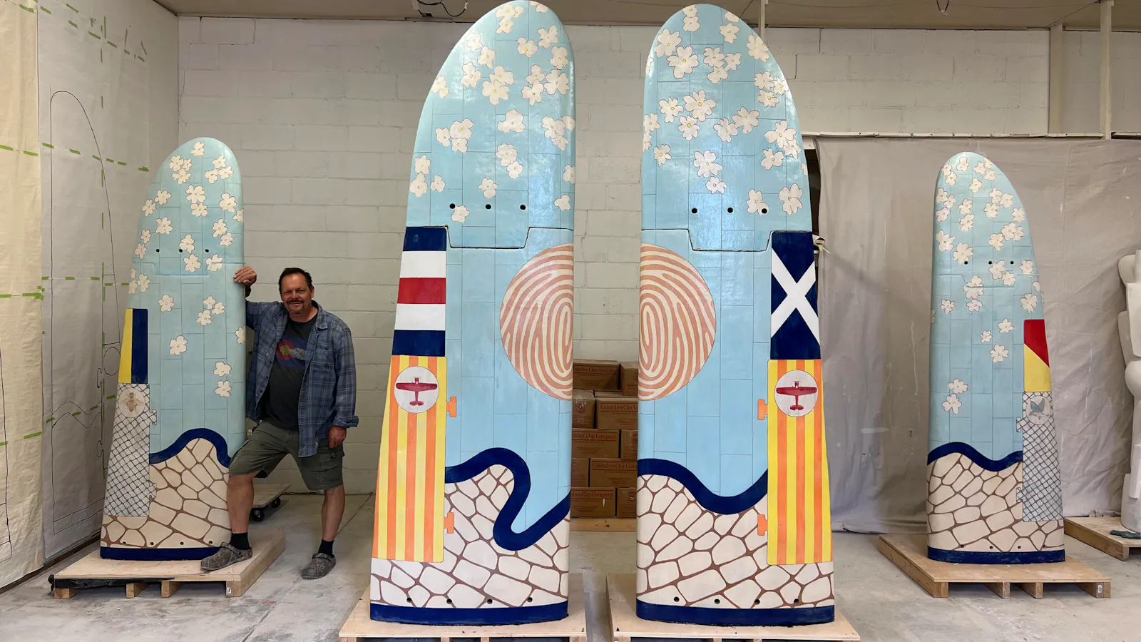 Artist John Balistreri stands smiling beside five colorful, upright sculptural panels prior to their installation at Kansas City International Airport