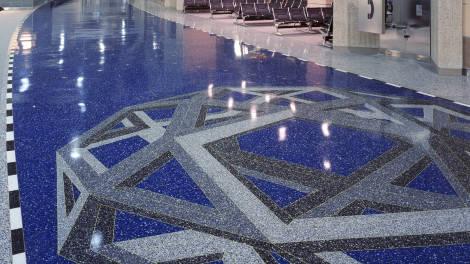 Geometric floor mosaic in a terminal at Kansas City International Airport, with interlocking gray and black shapes on a blue speckled surface.