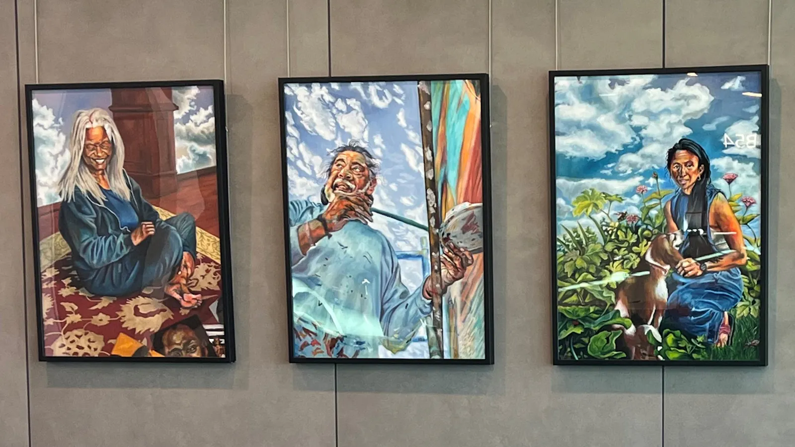 Five colorful portrait paintings hanging on a wall at Kansas City International Airport, each depicting a different person in outdoor or natural settings