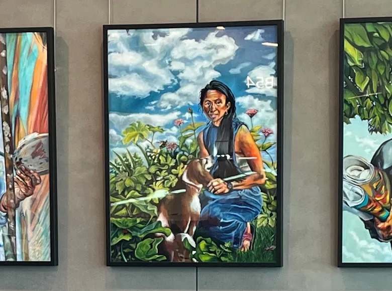 Five colorful portrait paintings hanging on a wall at Kansas City International Airport, each depicting a different person in outdoor or natural settings