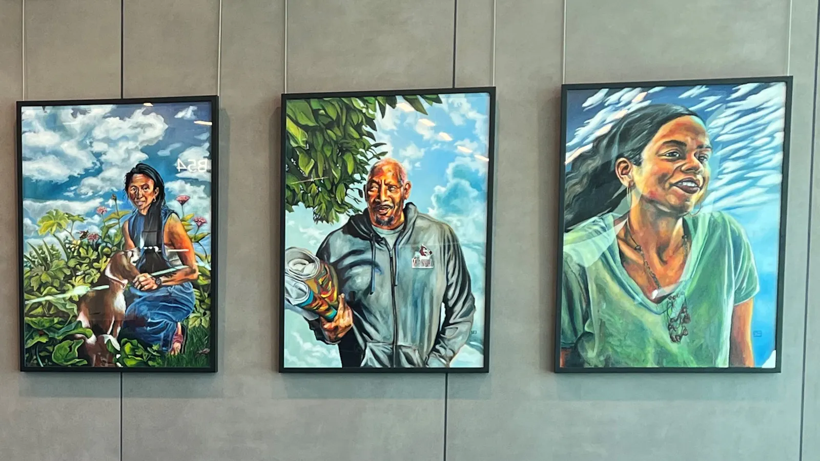 Five colorful portrait paintings hanging on a wall at Kansas City International Airport, each depicting a different person in outdoor or natural settings