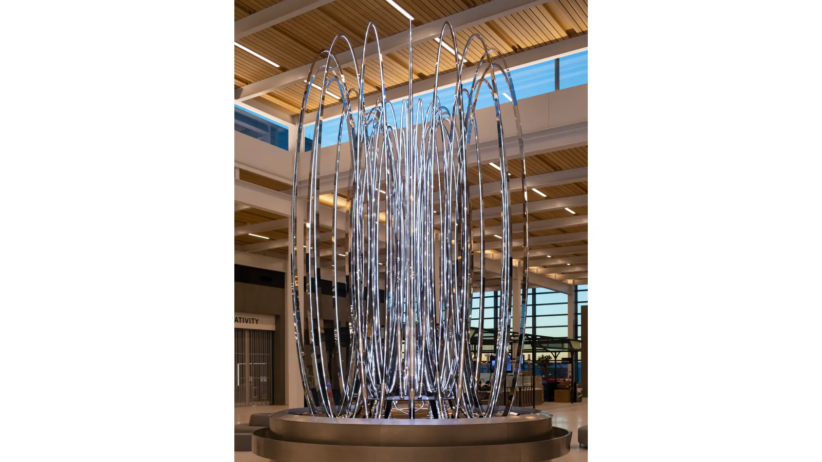 Vertical view of a glowing sculpture made of concentric metal loops on a circular base at Kansas City International Airport.