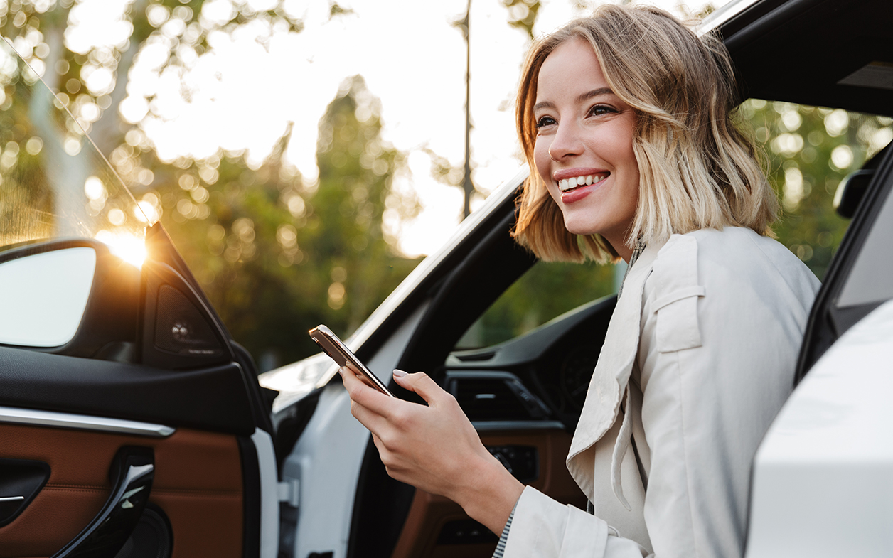 Smiling young woman holding her phone getting out of her car