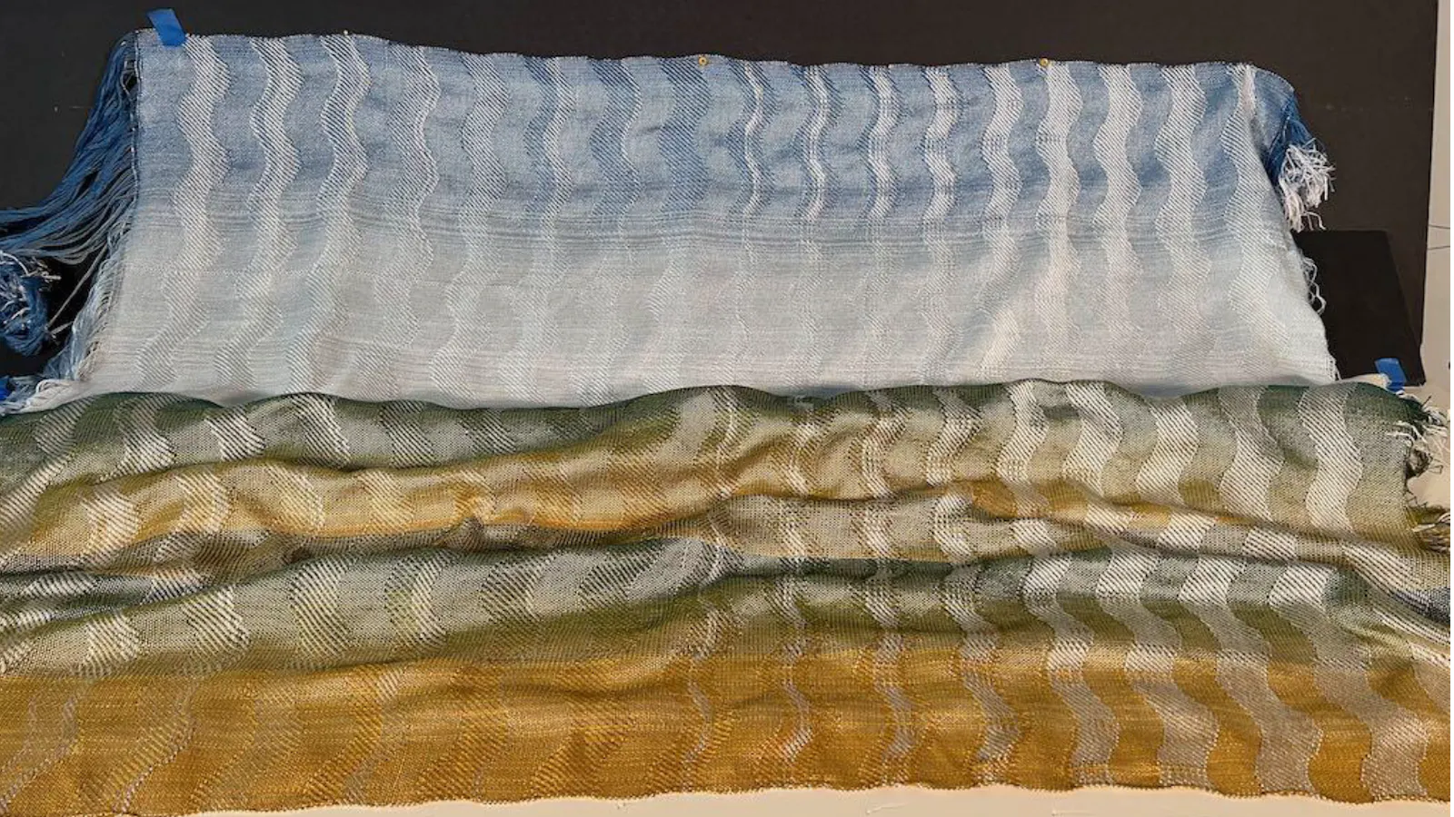 Two handwoven textile panels laid side by side, featuring soft gradient hues from blue to green and gold with a subtle wave-like pattern.