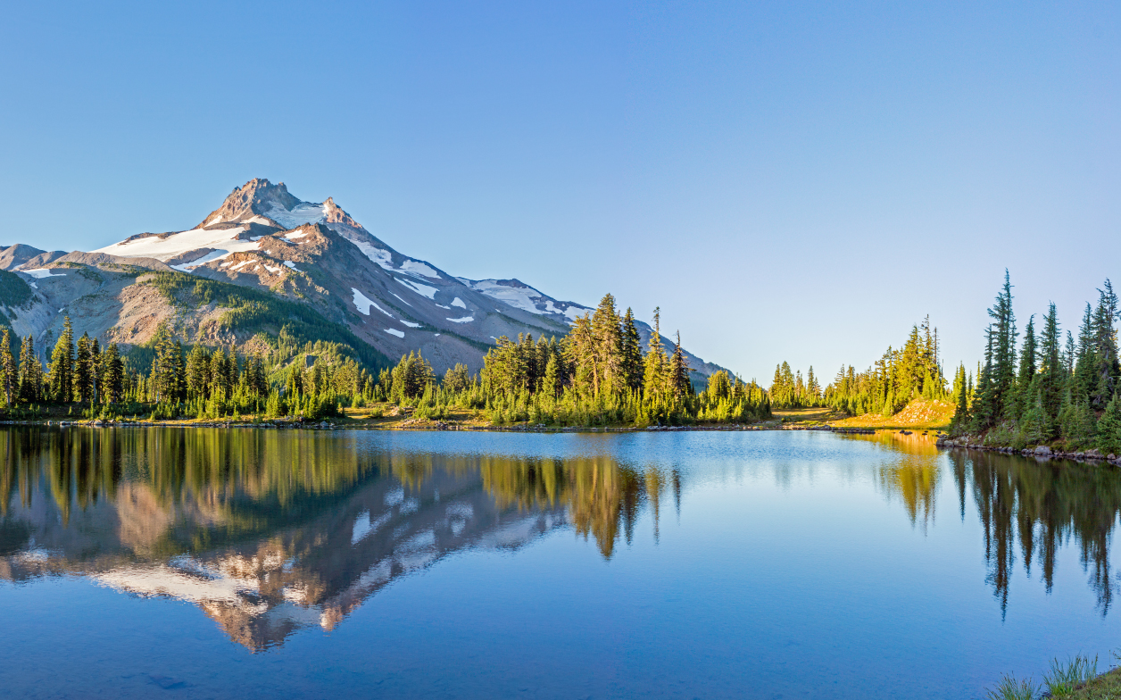 Photo of mountain and calm lake during summer against a clear blue sky